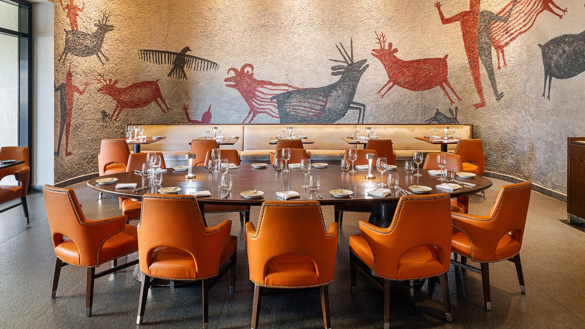 a table with orange chairs and a wall with drawings on the wall
