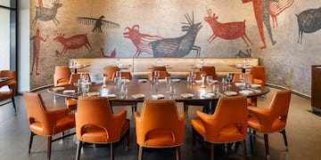a table with orange chairs and a wall with drawings on the wall