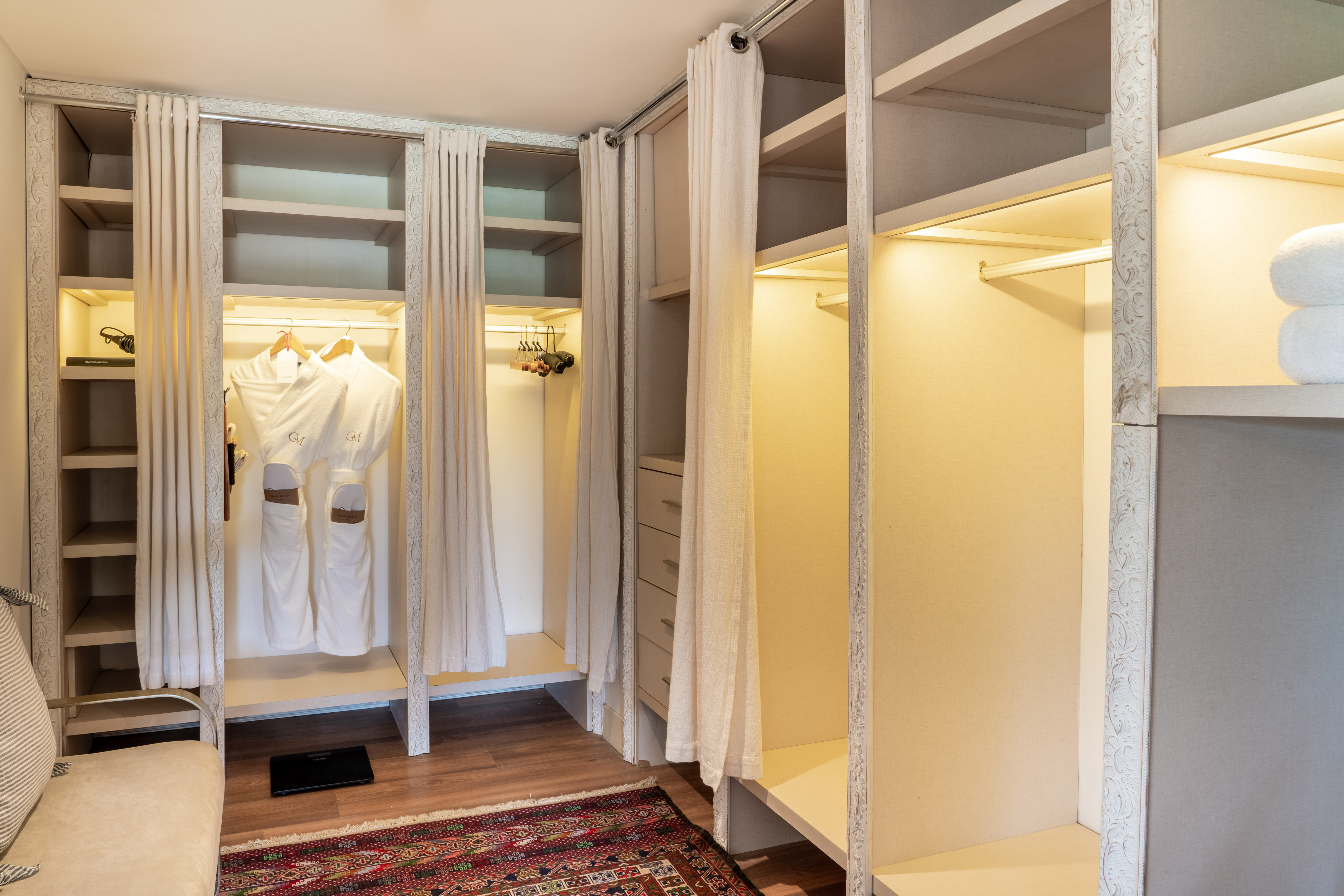 Hotel closet with bathrobes, shelves, white drapes, and integrated lighting.
