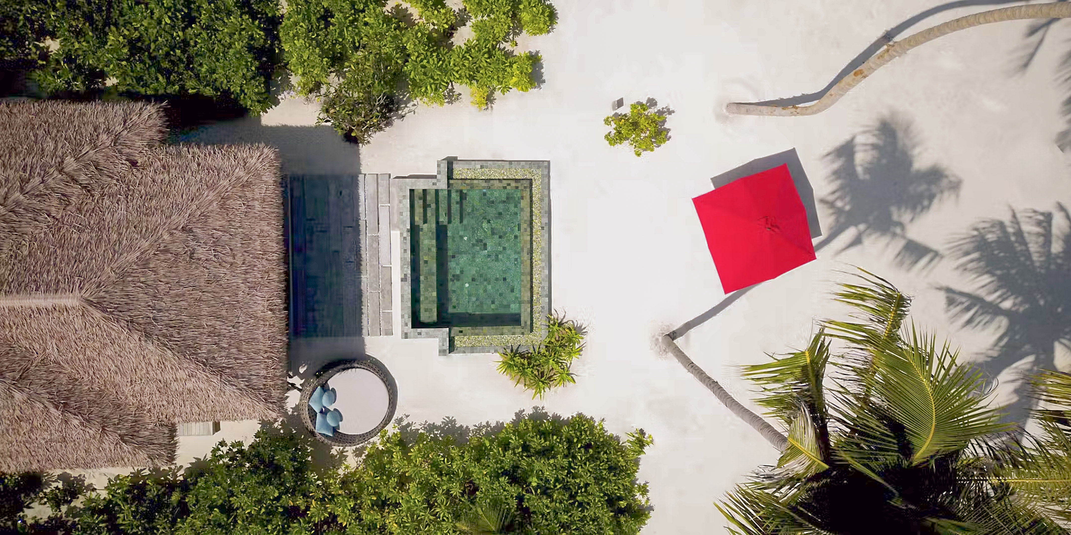 Tropical villa with private pool, thatched roof, red umbrella on white sand.