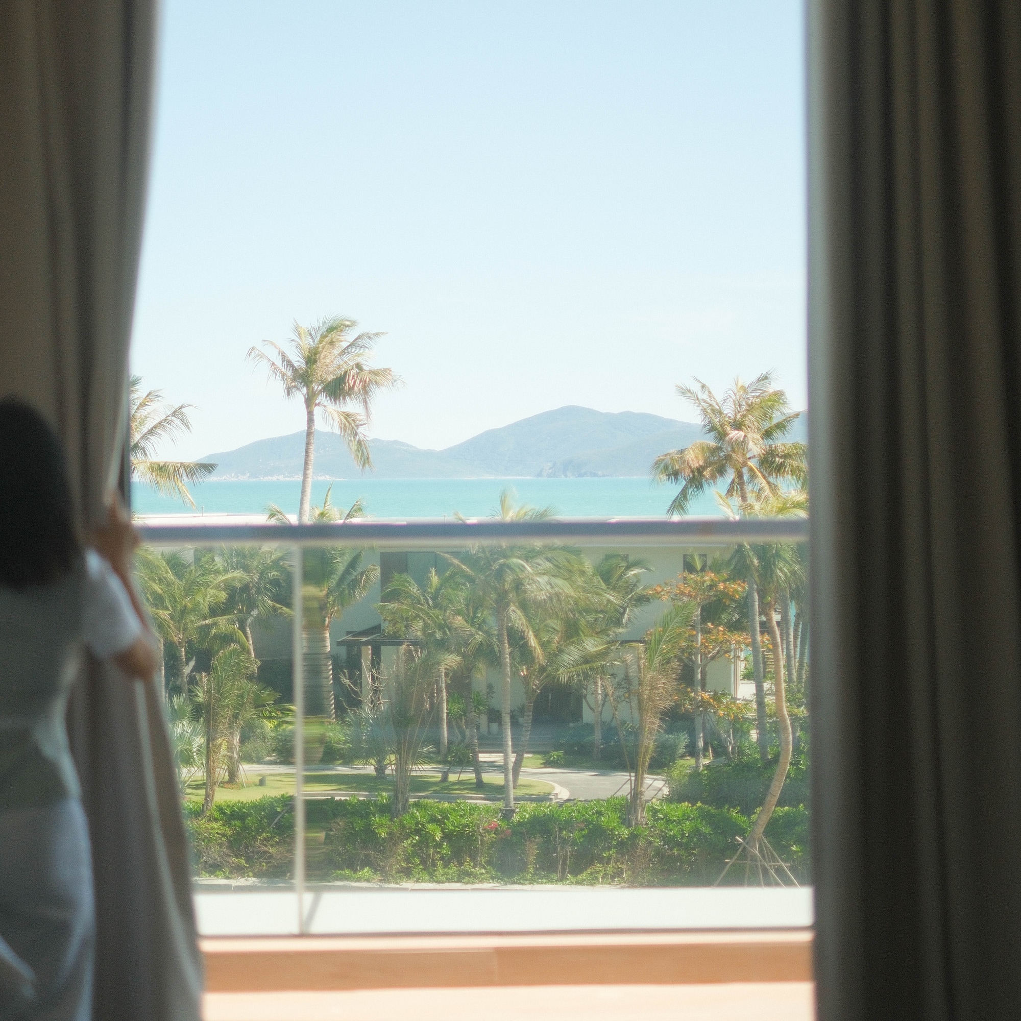 a person looking out a window at a tropical resort