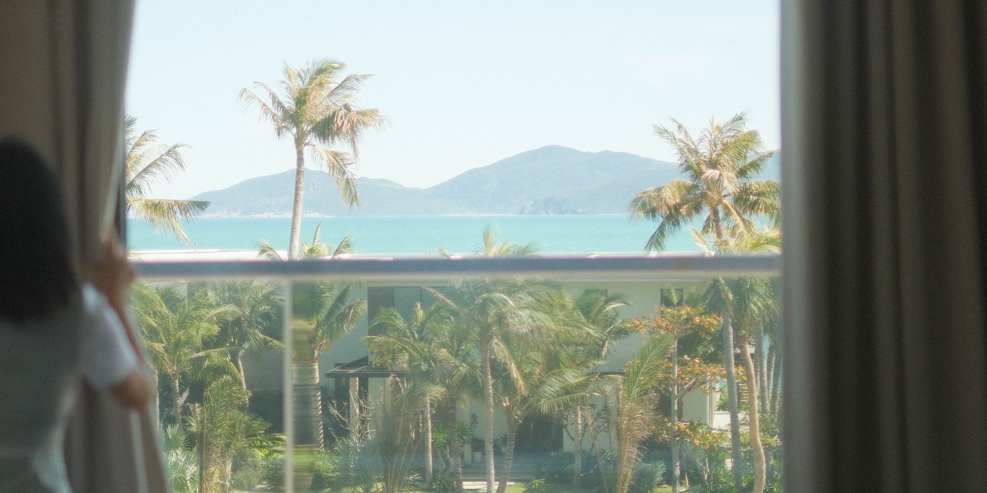 a person looking out a window at a tropical resort