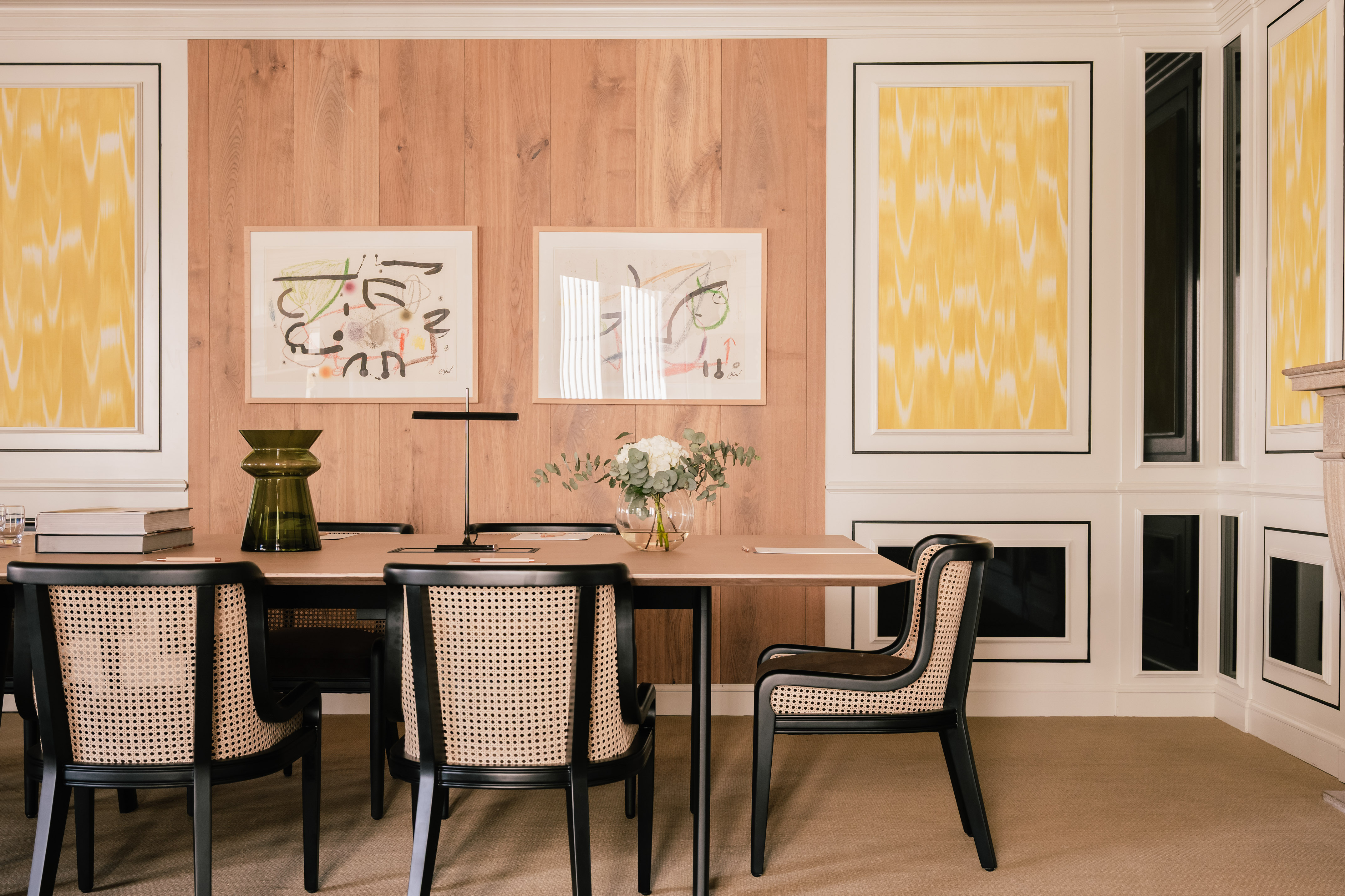 Modern dining room with wood paneling, abstract art, and black cane chairs.