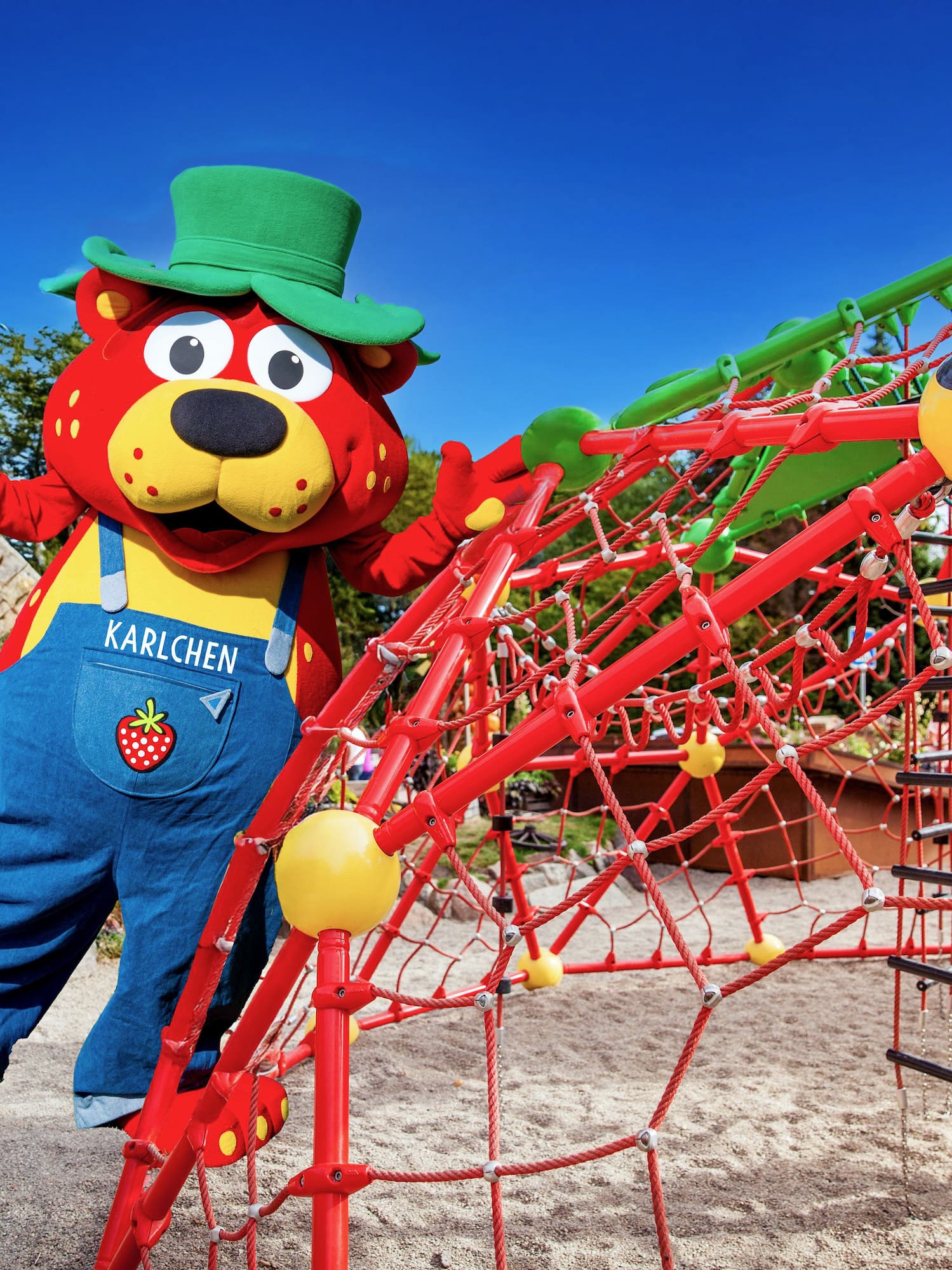 Karlchen bear mascot in green hat on adventure playground structure.