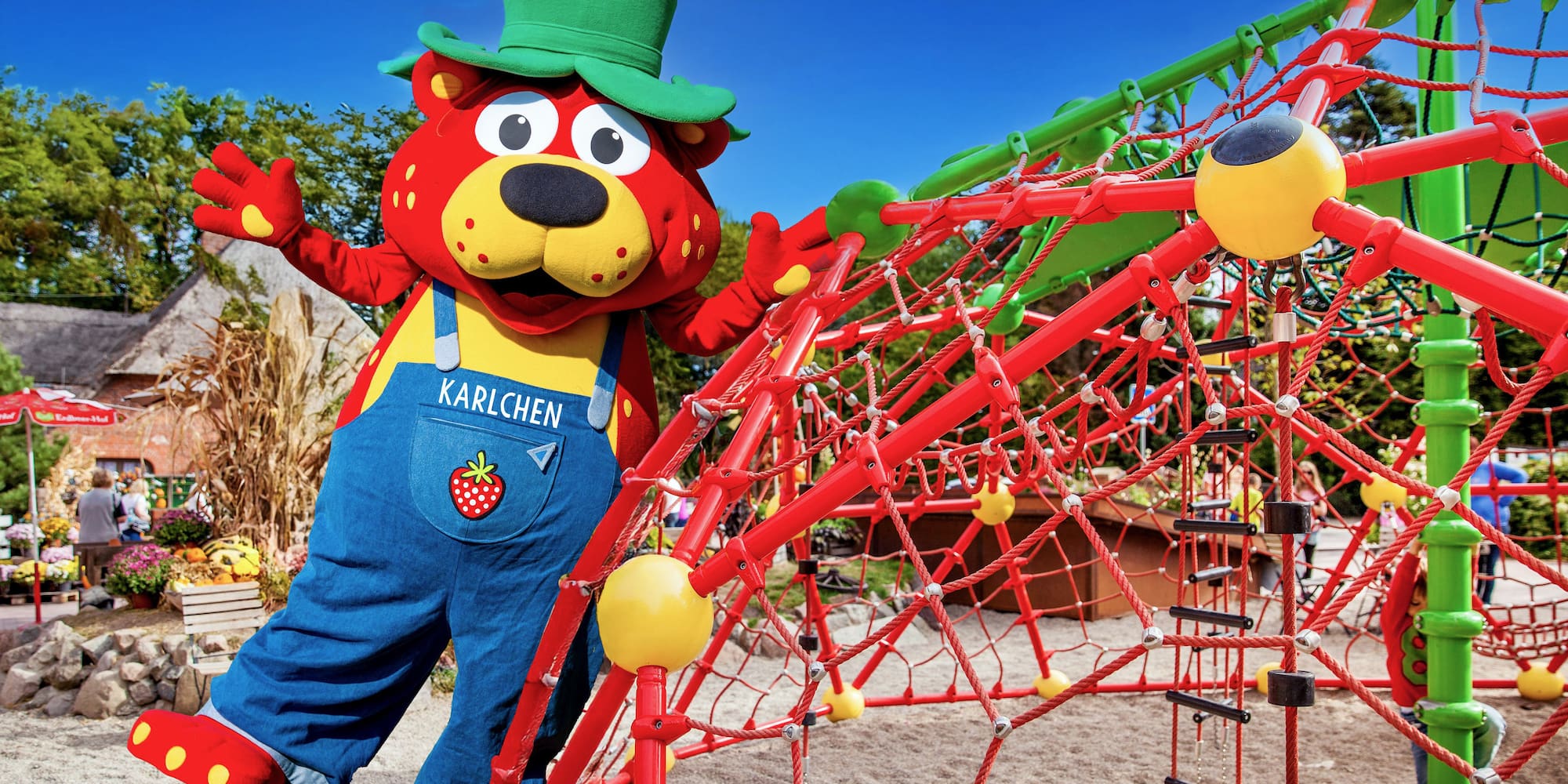 Karlchen strawberry mascot on a vibrant red and green playground climber.