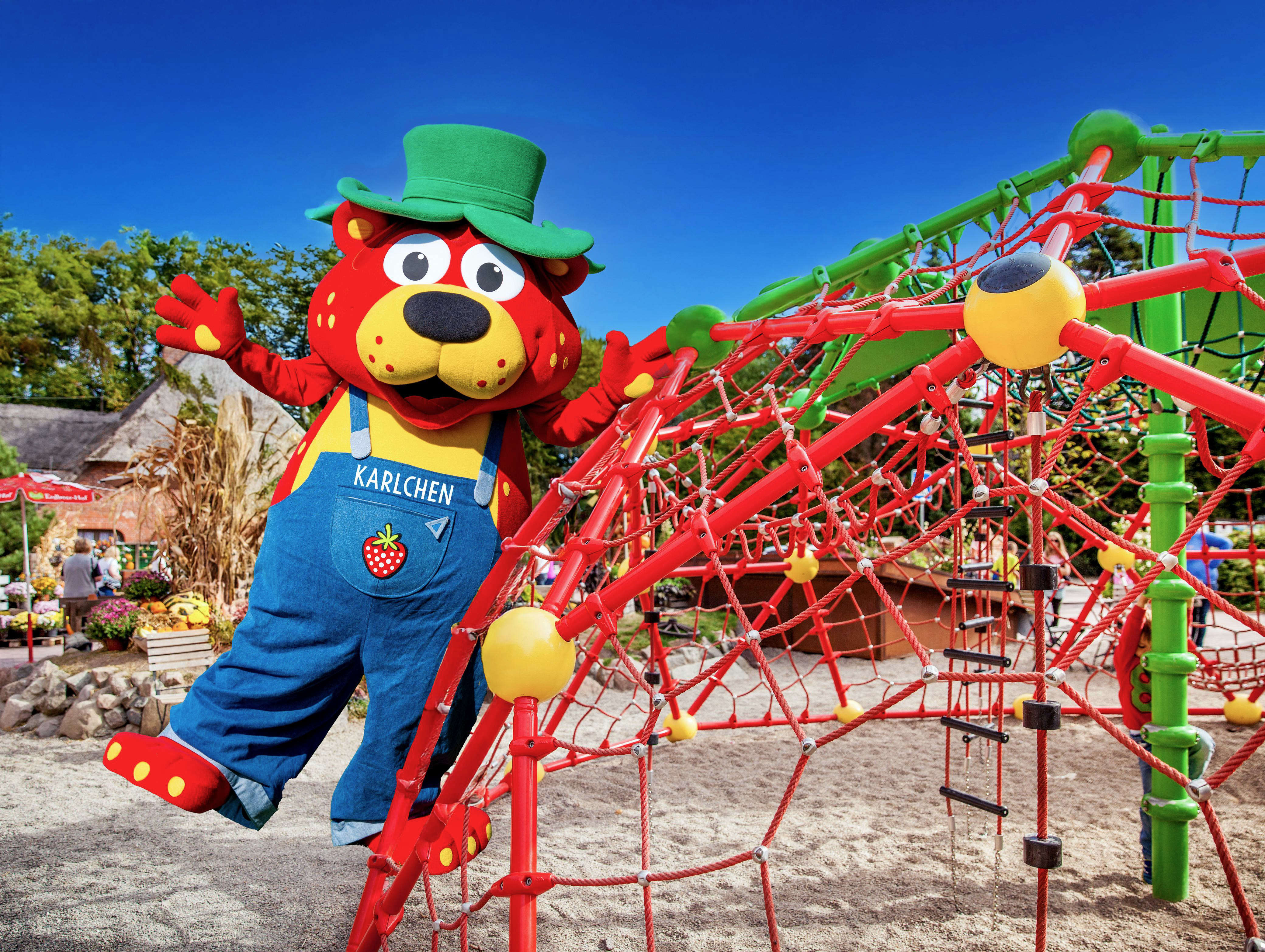 Karlchen strawberry mascot on a vibrant red and green playground climber.