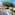 Balcony with white table, chairs, blue railing, street view, and large pine tree.