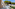 Balcony with white table, chairs, blue railing, street view, and large pine tree.