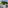Balcony with white table, chairs, blue railing, street view, and large pine tree.