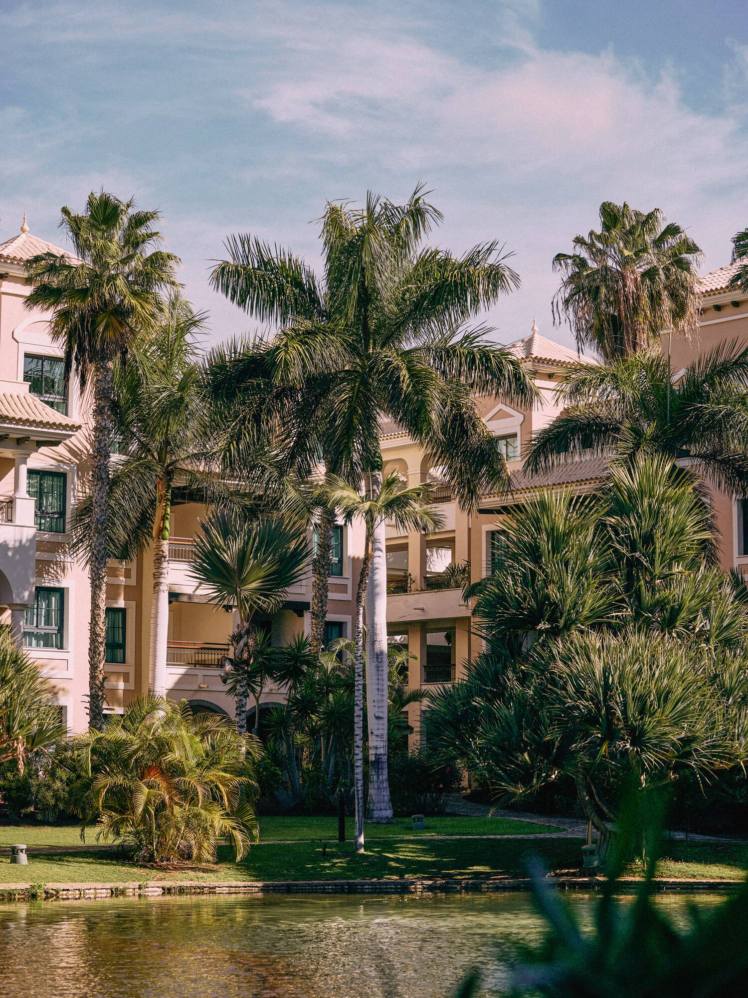 Hotel resort con palmeras, jardines exuberantes y estanque. Ambiente tropical.