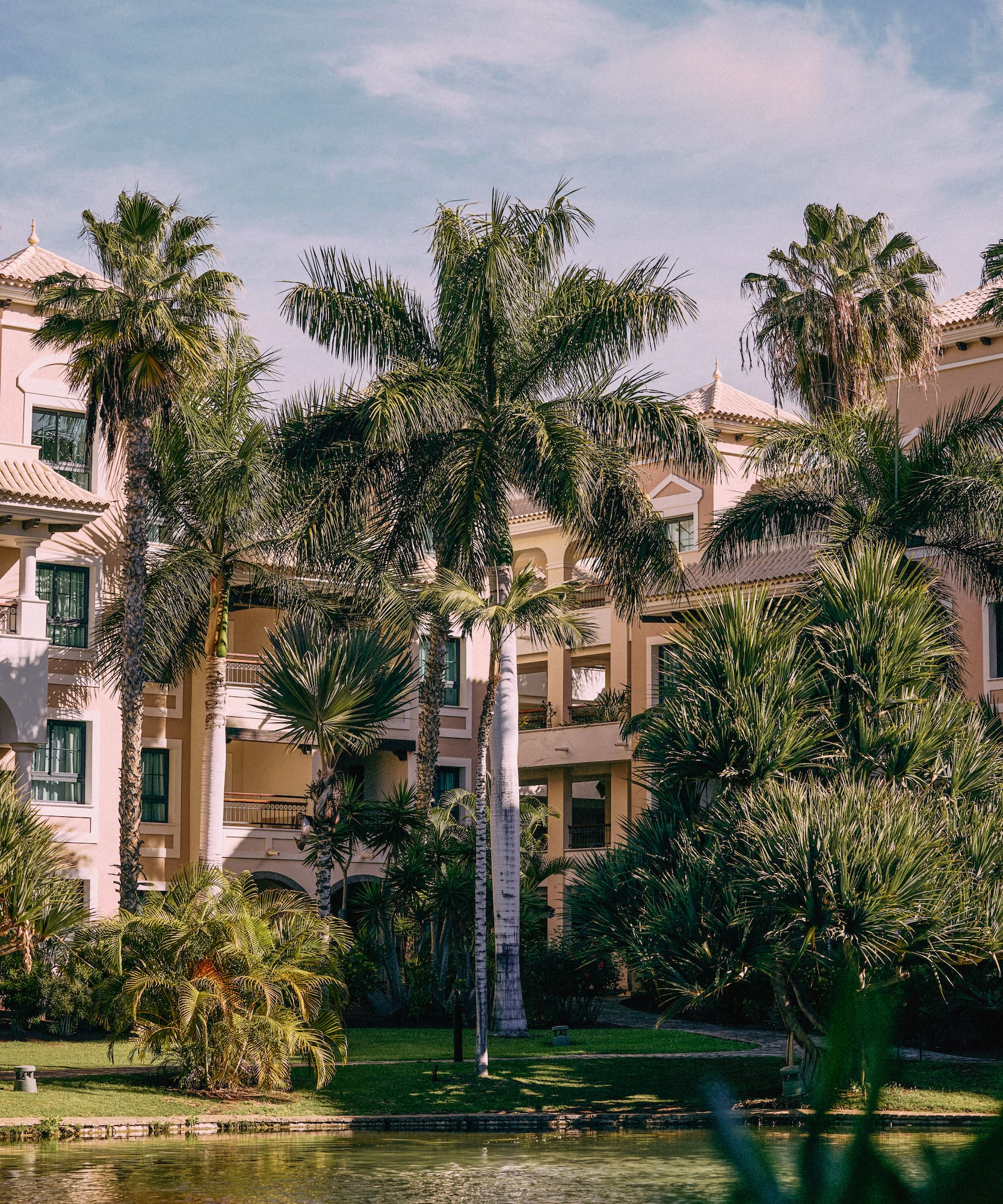 Hotel resort con palmeras, jardines exuberantes y estanque. Ambiente tropical.