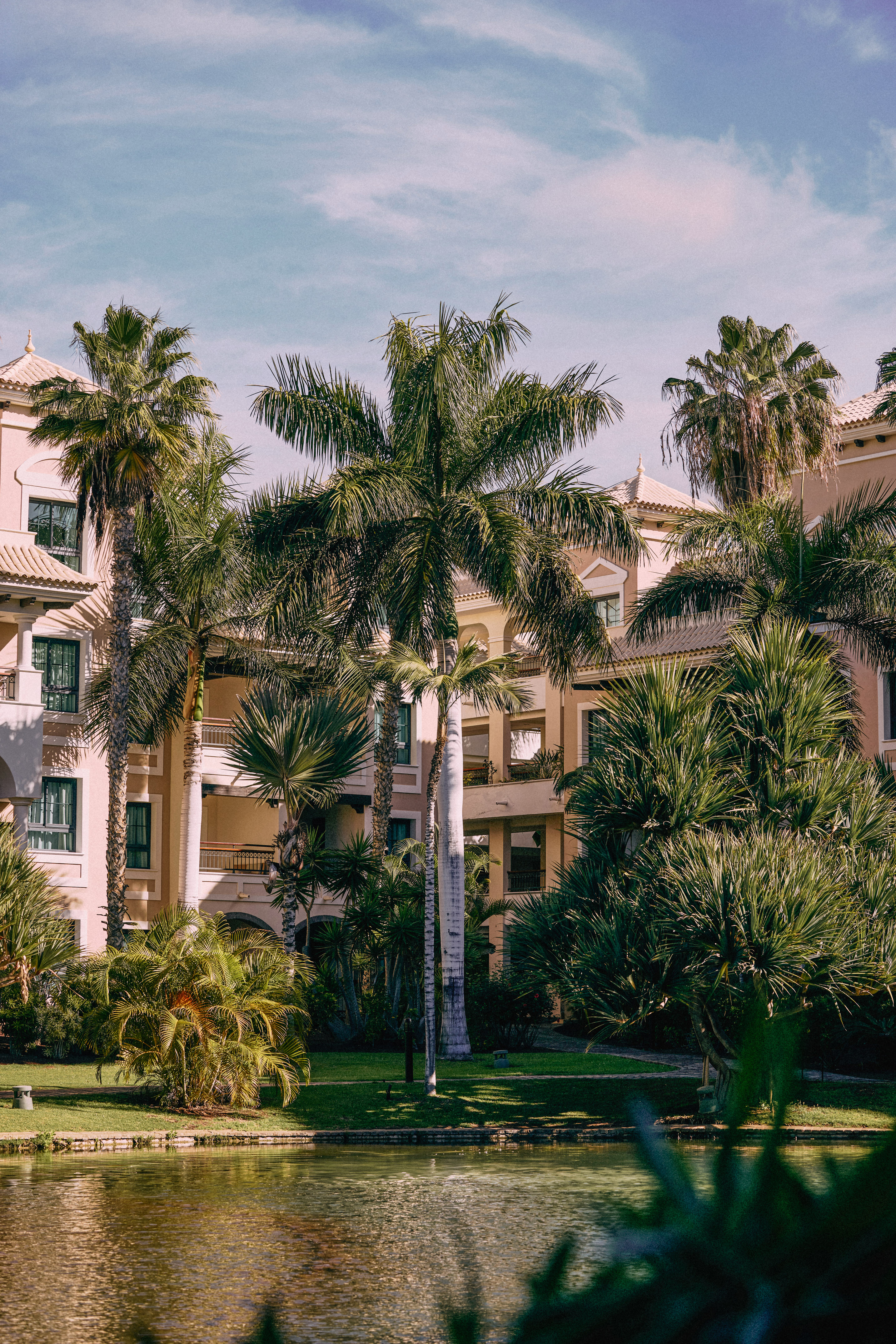 Hotel resort con palmeras, jardines exuberantes y estanque. Ambiente tropical.