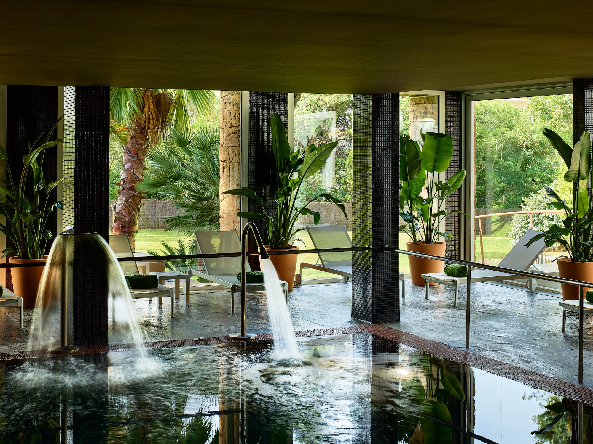 Spa con piscina interior, chorros de agua, jardín y tumbonas.