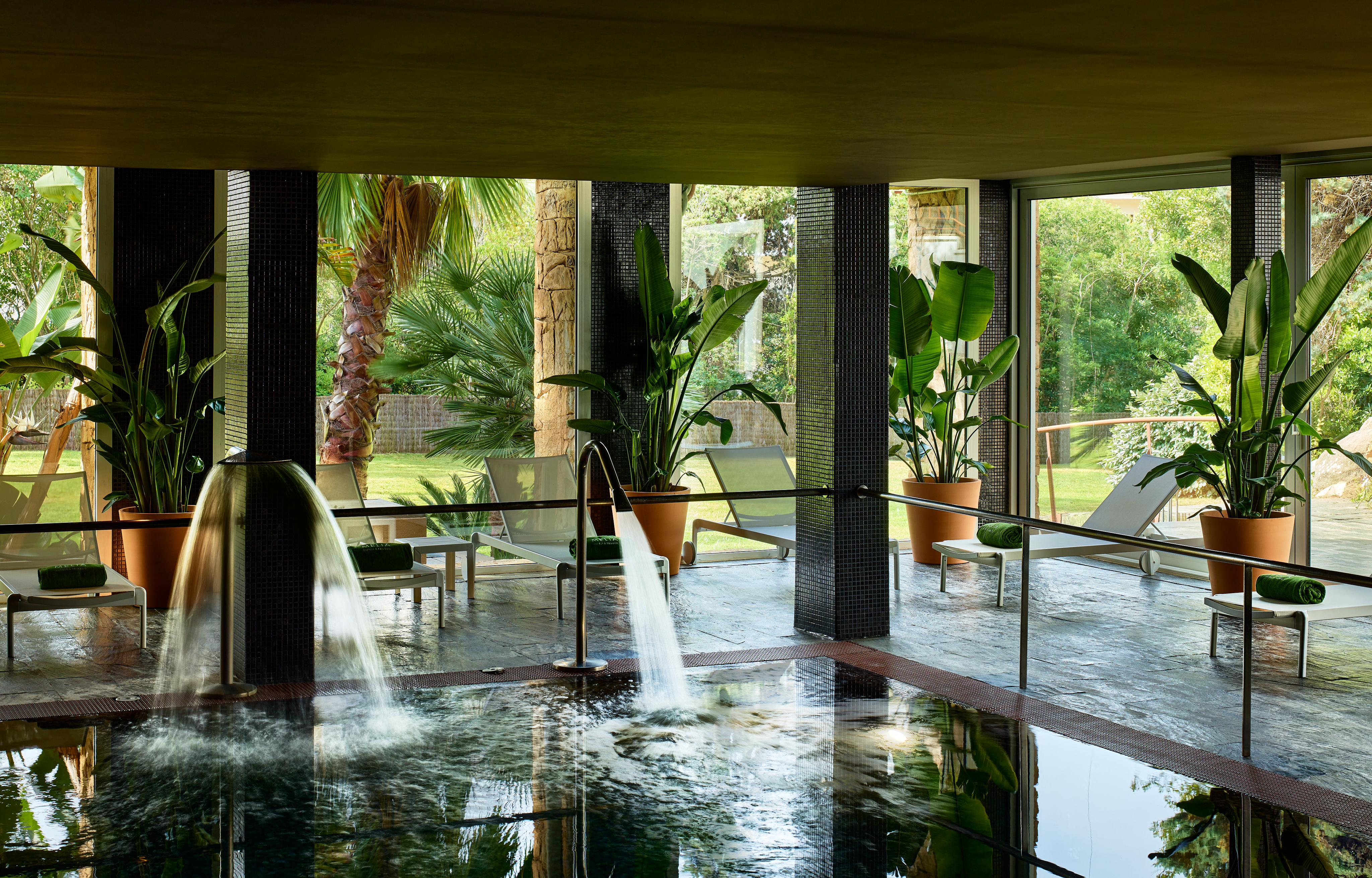 Spa con piscina interior, chorros de agua, jardín y tumbonas.