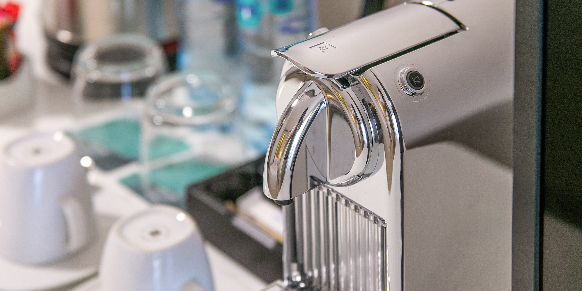 Chrome Nespresso coffee machine with cups and bottled water in a hotel room.