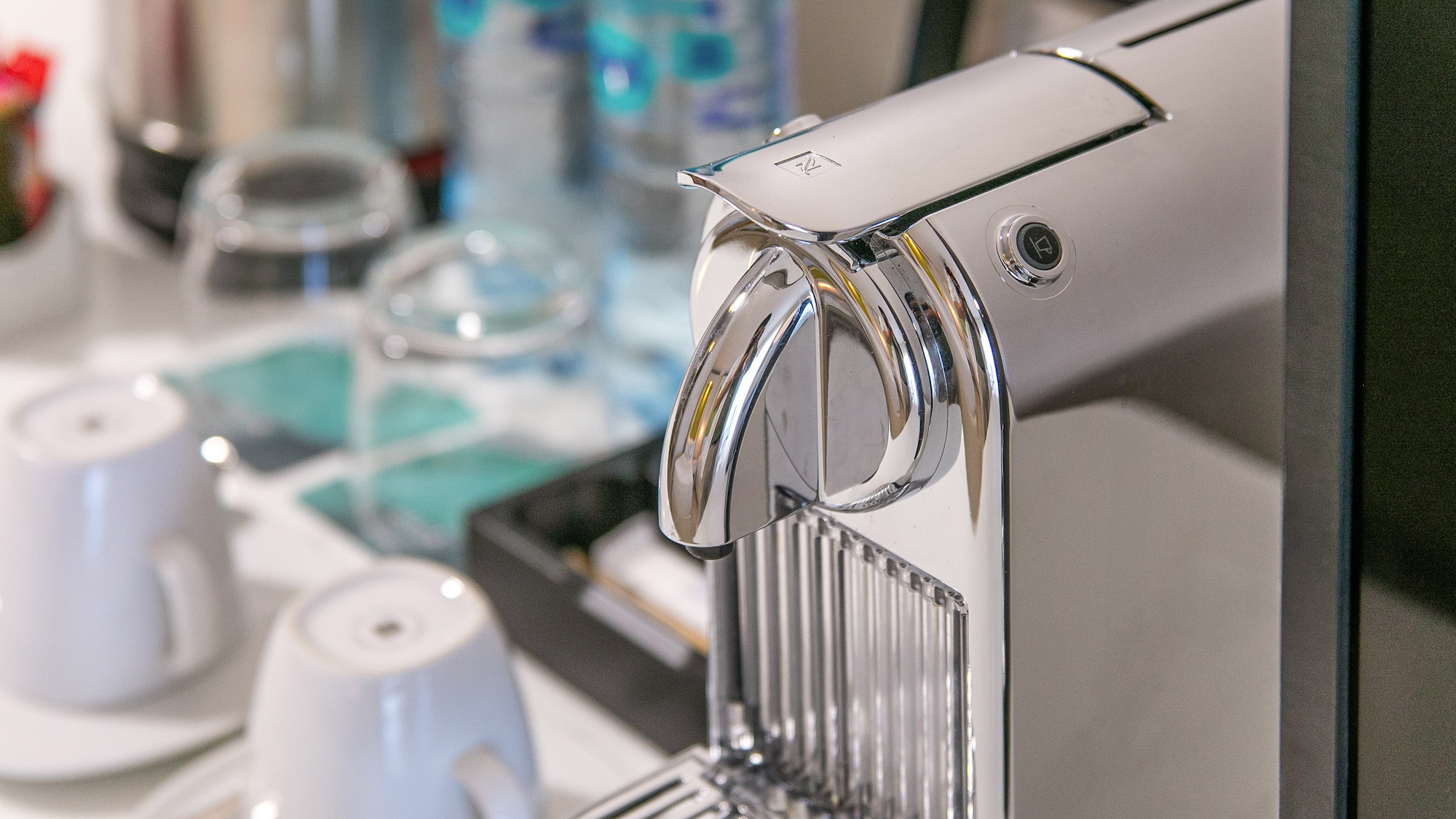 Chrome Nespresso coffee machine on a hotel tray with cups and water bottles.
