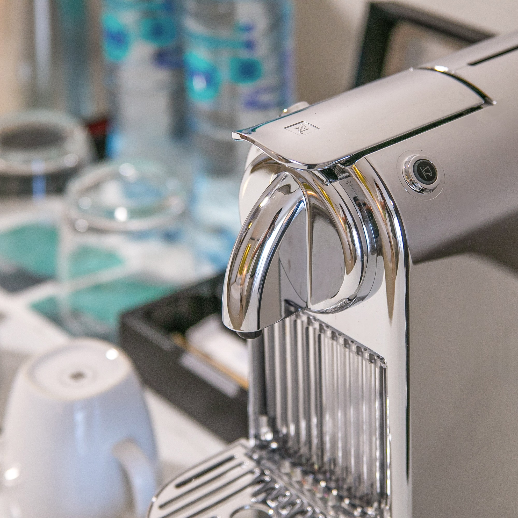 Chrome Nespresso coffee machine with cups and bottled water in a hotel room.