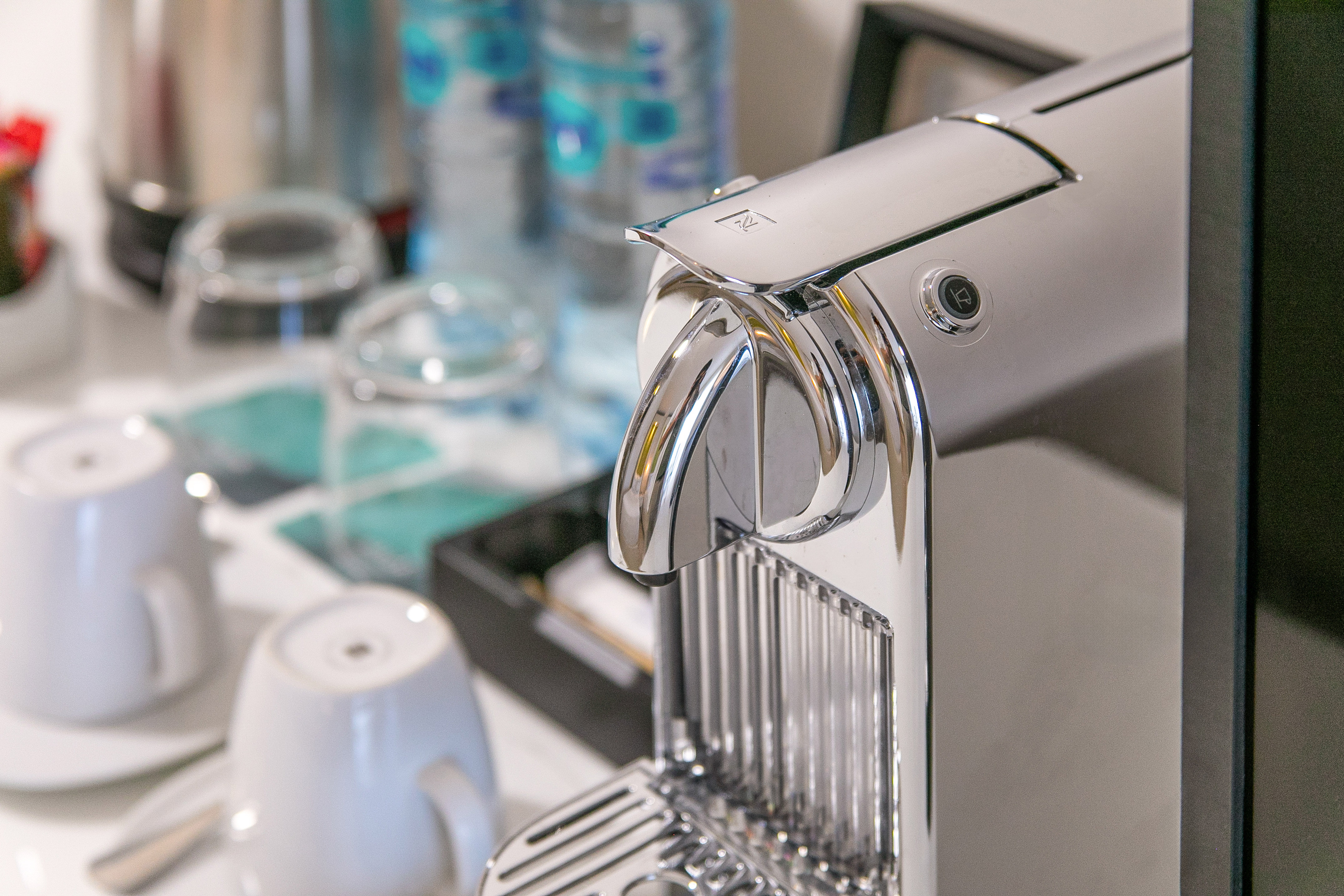 Chrome Nespresso coffee machine with cups and bottled water in a hotel room.