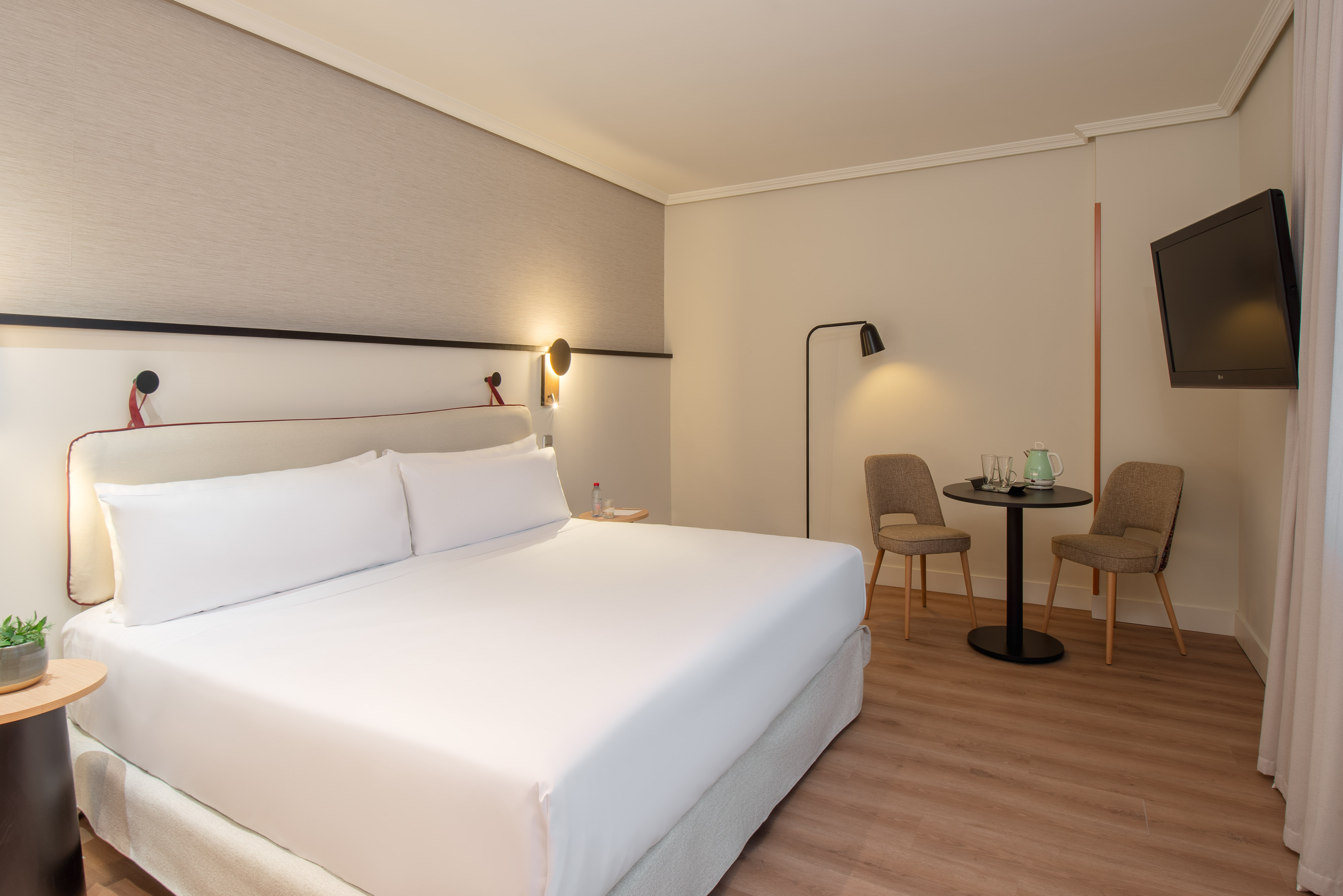 Modern hotel room with king-size bed, table with chairs, and wall-mounted TV.