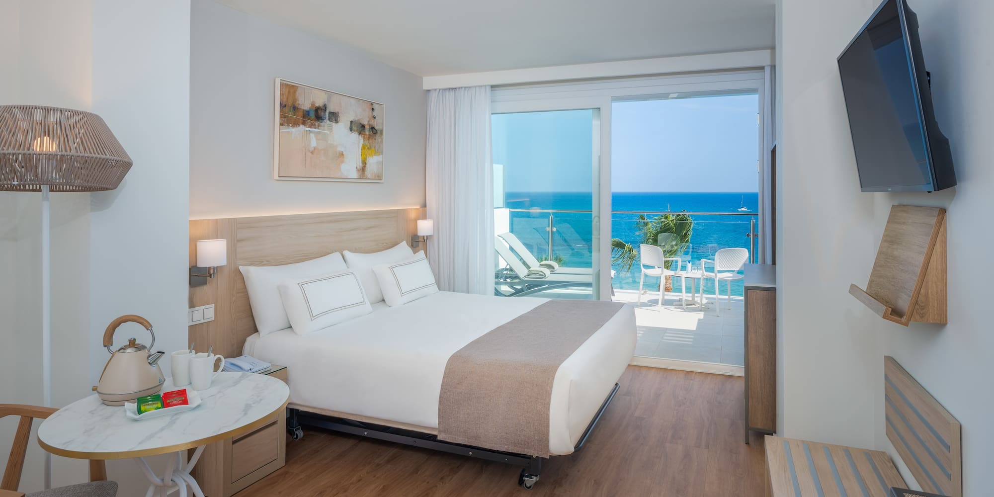 Modern hotel room with ocean view balcony, large bed, and stylish decor.