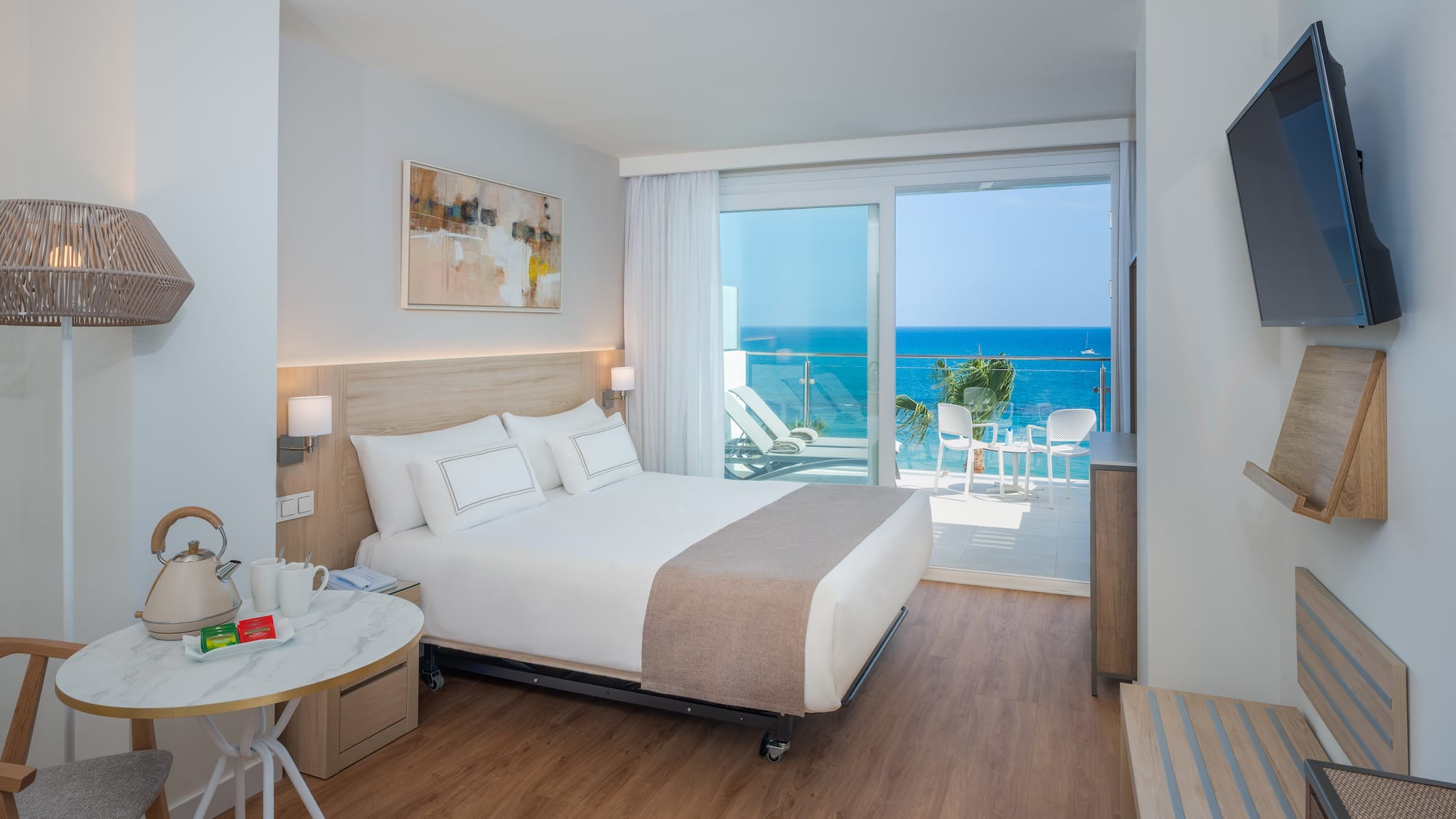 Modern hotel room with ocean view balcony, white bed, and wooden floor.