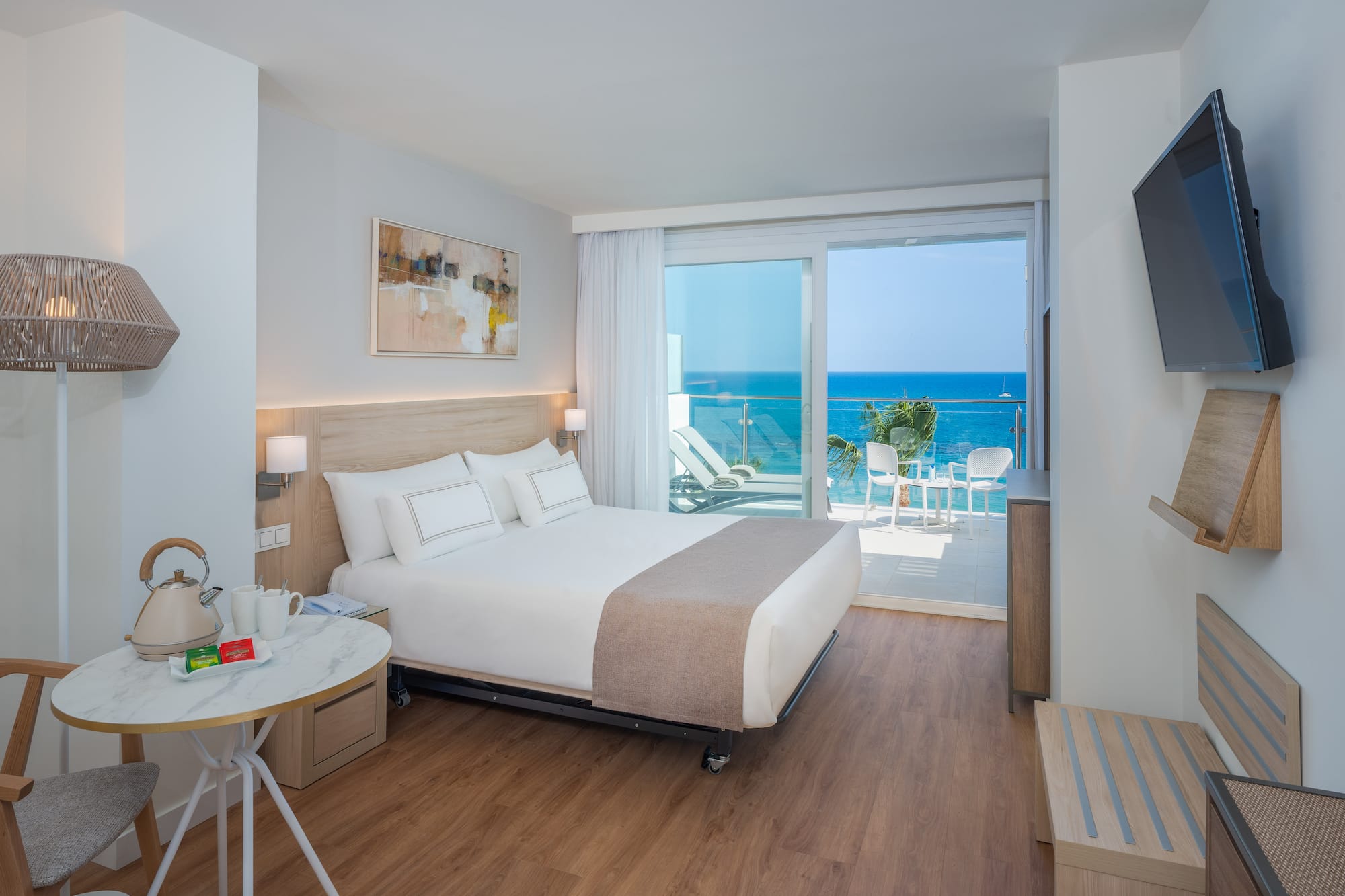 Modern hotel room with ocean view balcony, large bed, and stylish decor.