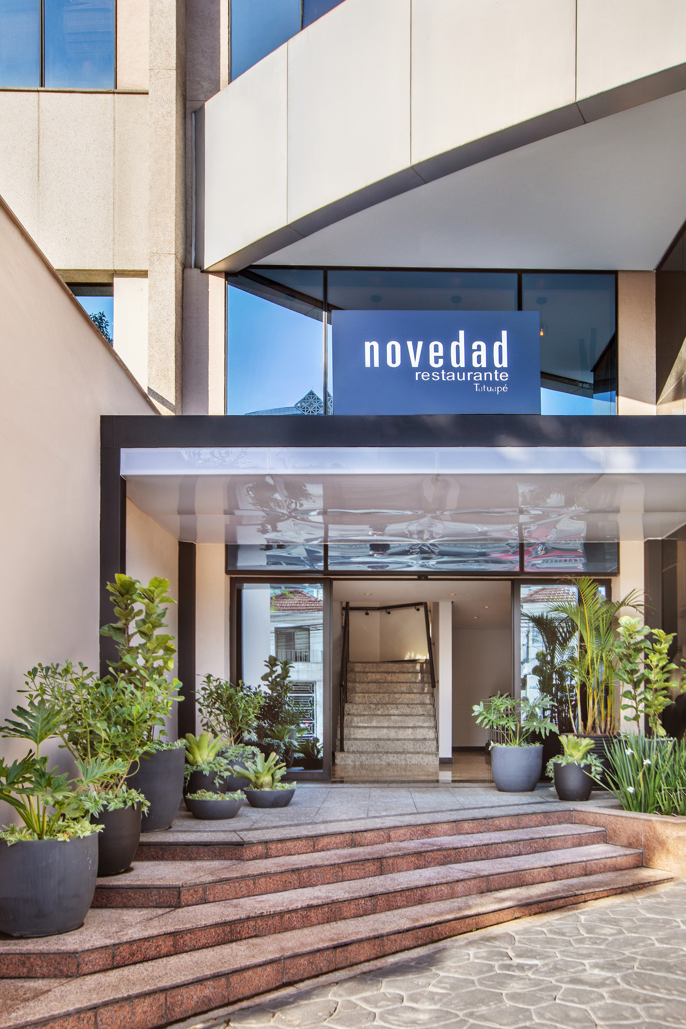 Modern Novedad Restaurante Tatuapé entrance with granite steps and potted greenery.