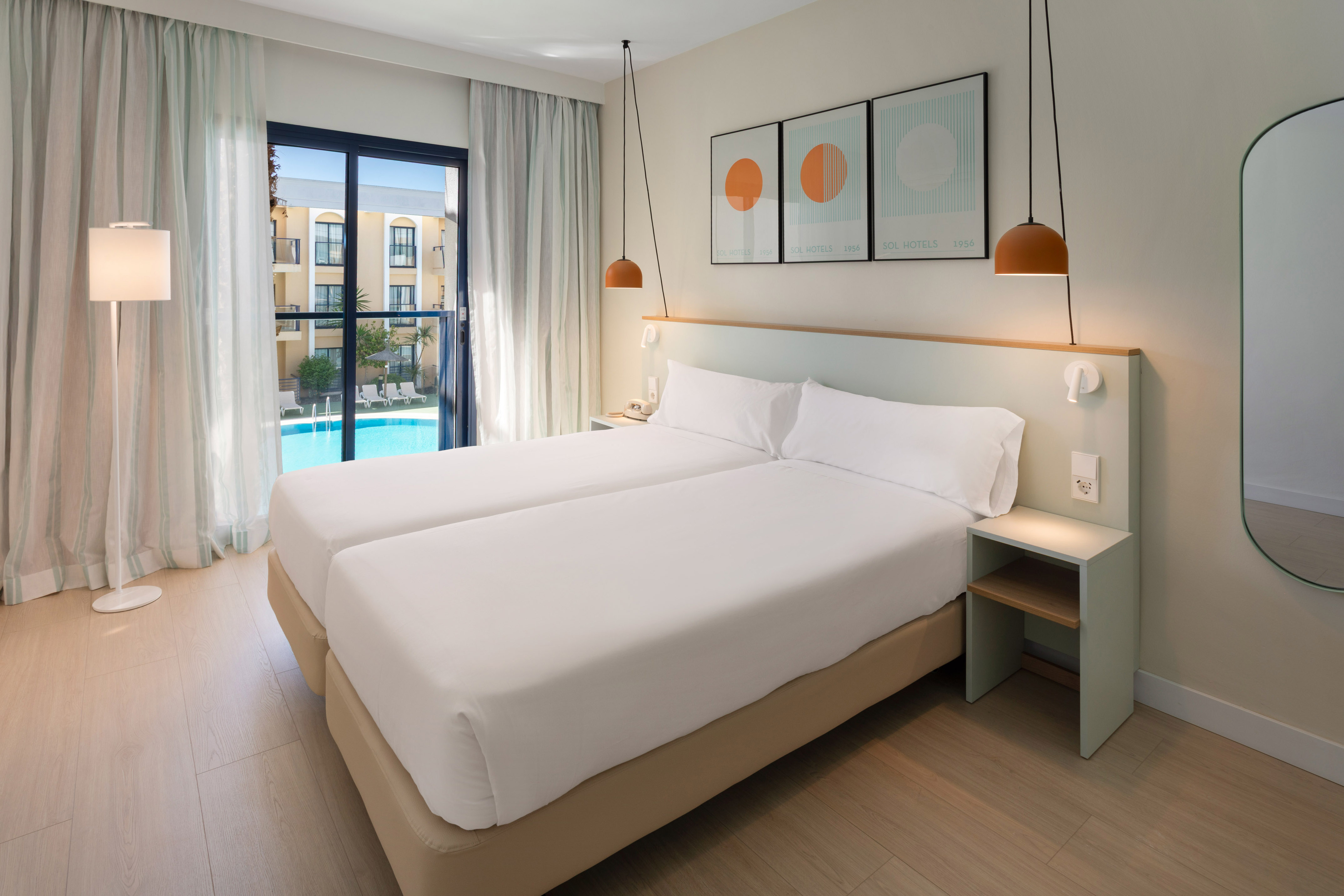 Bright hotel room with twin beds and resort pool view from balcony.