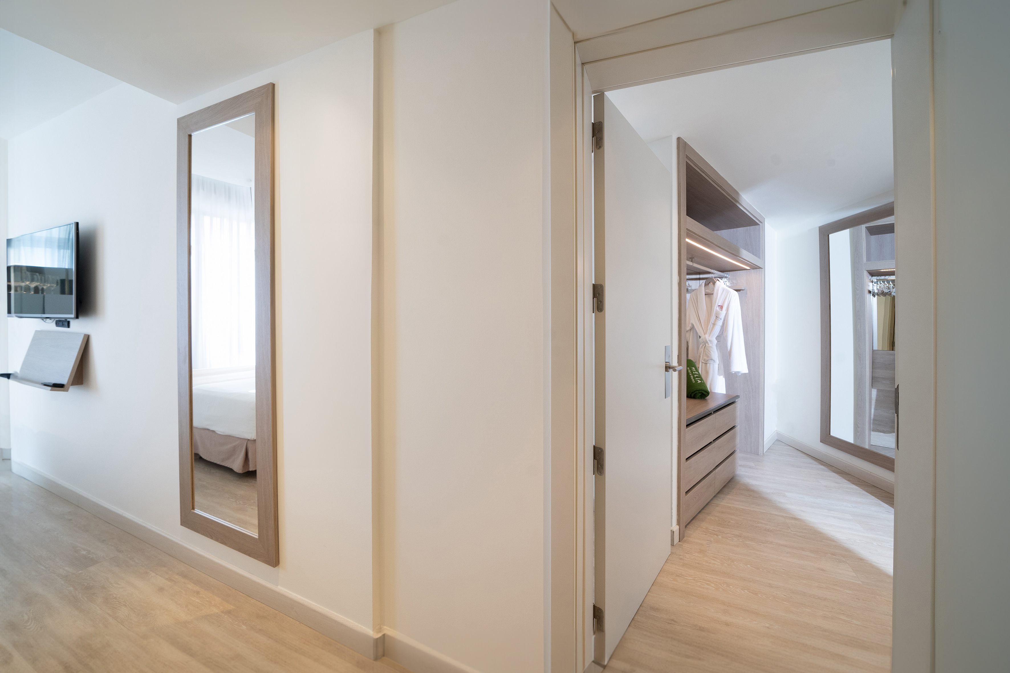 Modern hotel room with full-length mirror, wall-mounted TV, and walk-in closet.