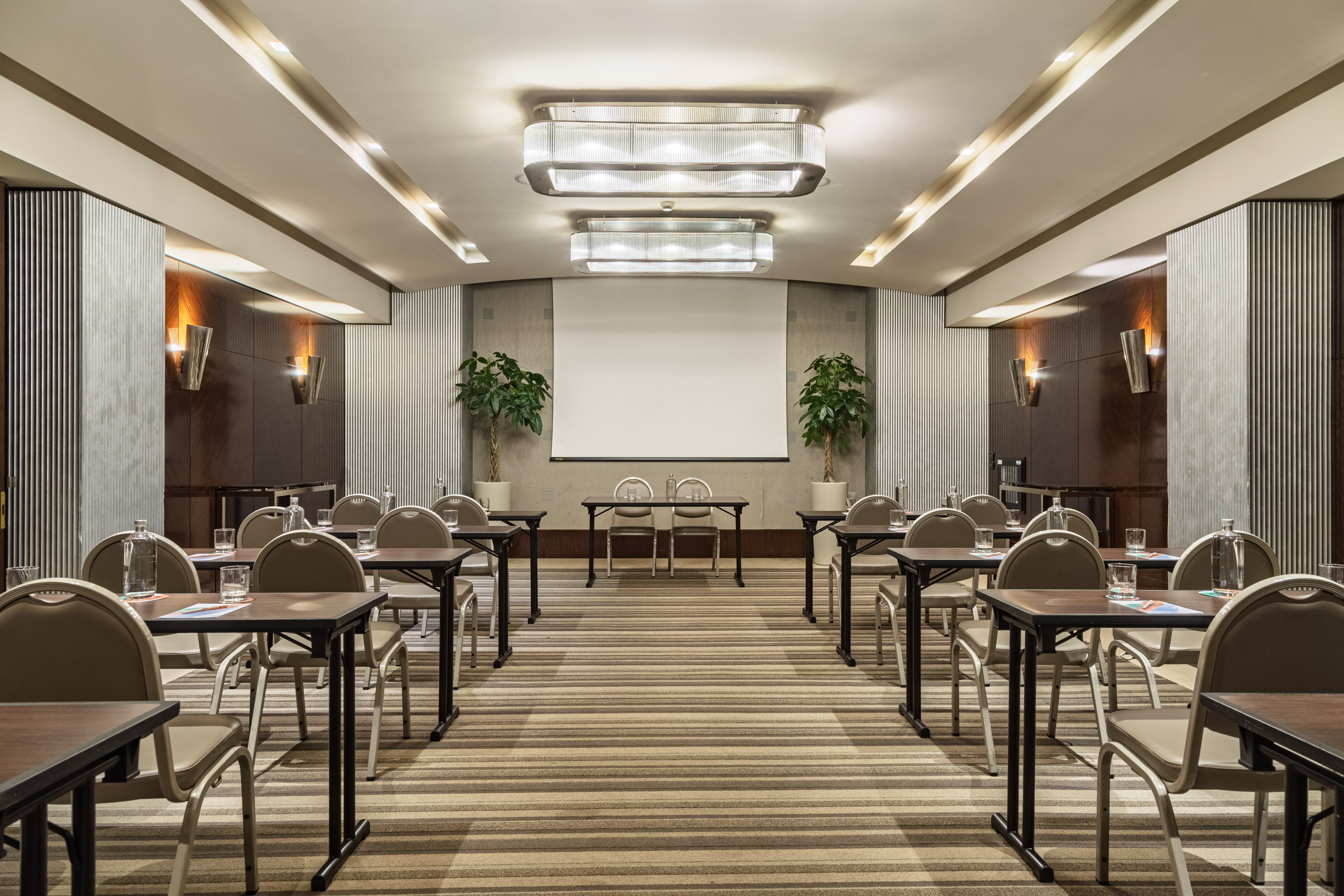 Modern conference room with tables, chairs, projection screen, and elegant lighting.