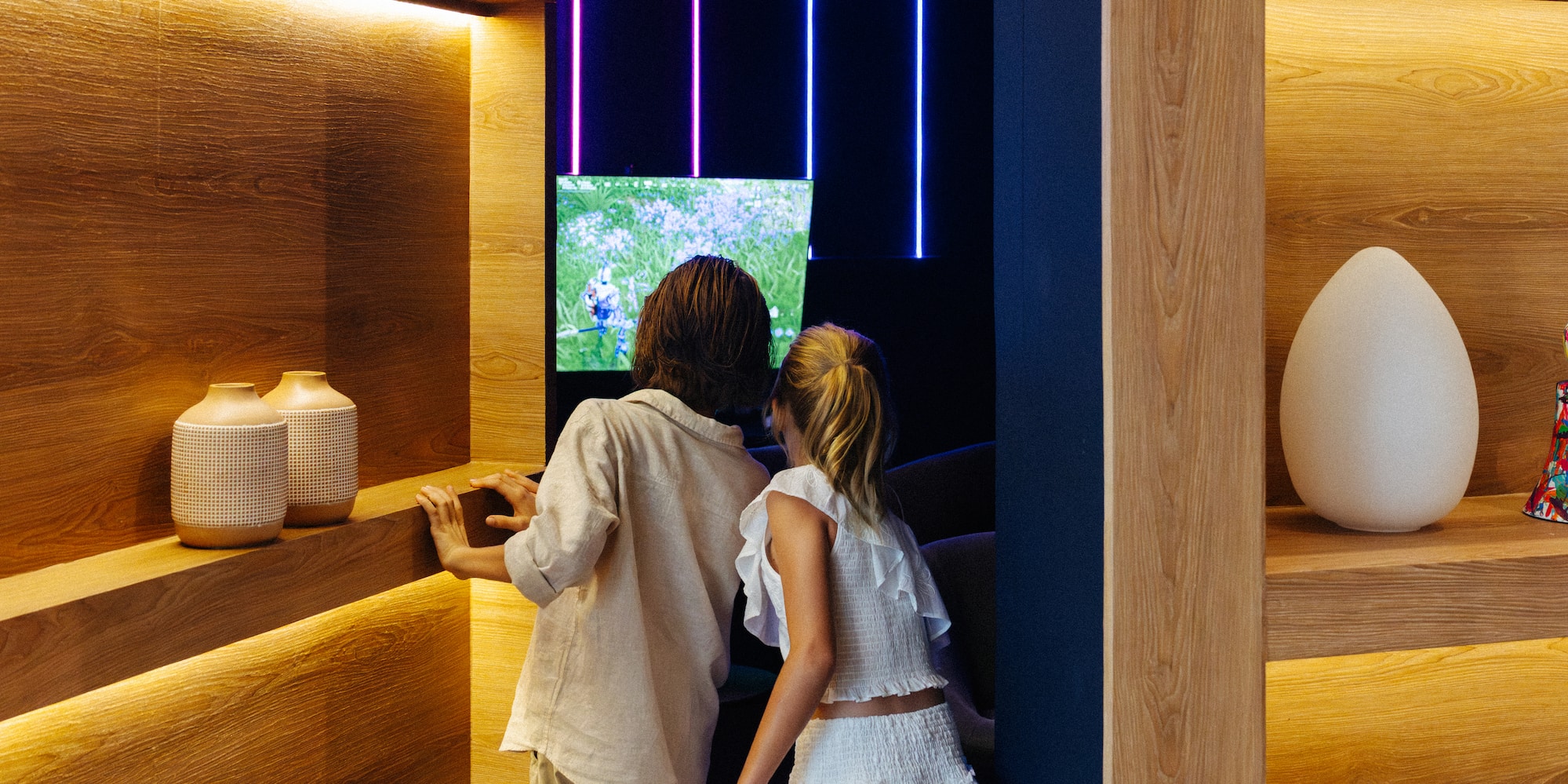 Kids watching screen in modern wooden room with neon and LED lights.