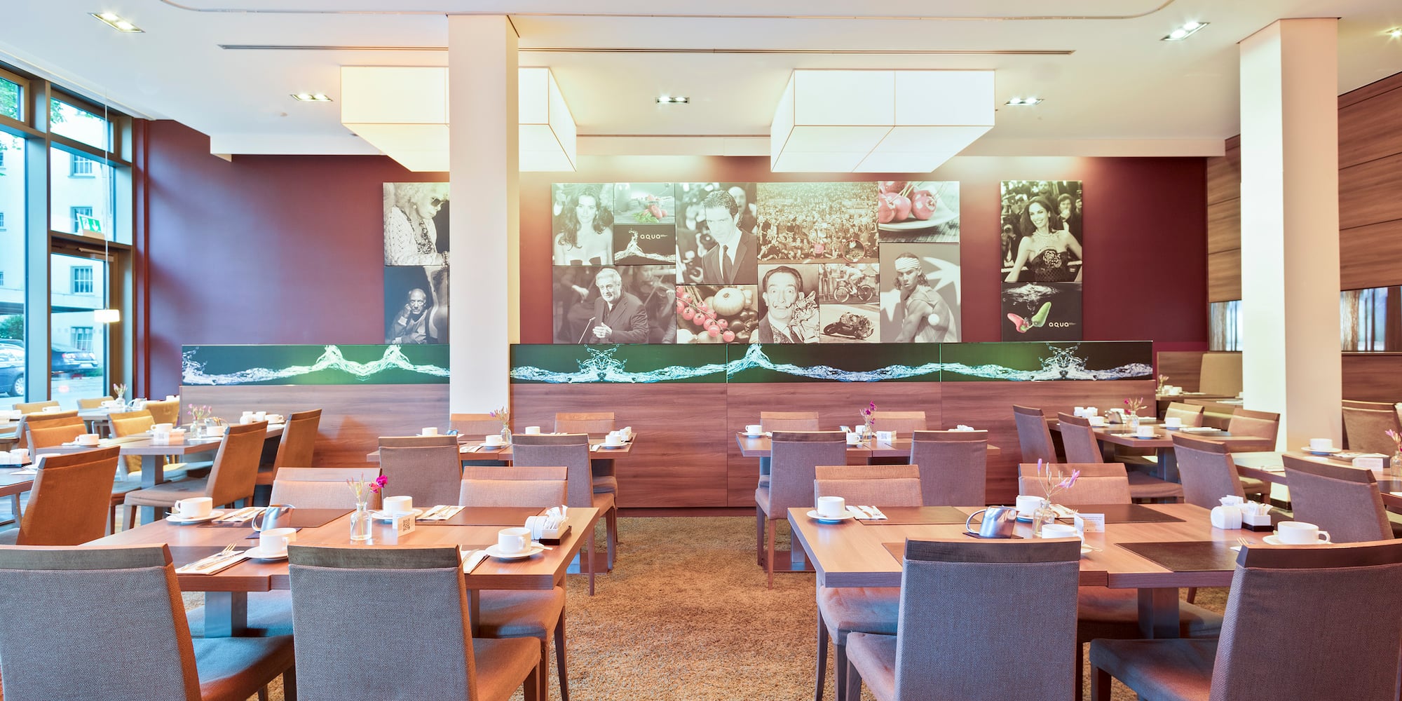 Modern hotel restaurant with set tables, maroon walls, and artistic murals.