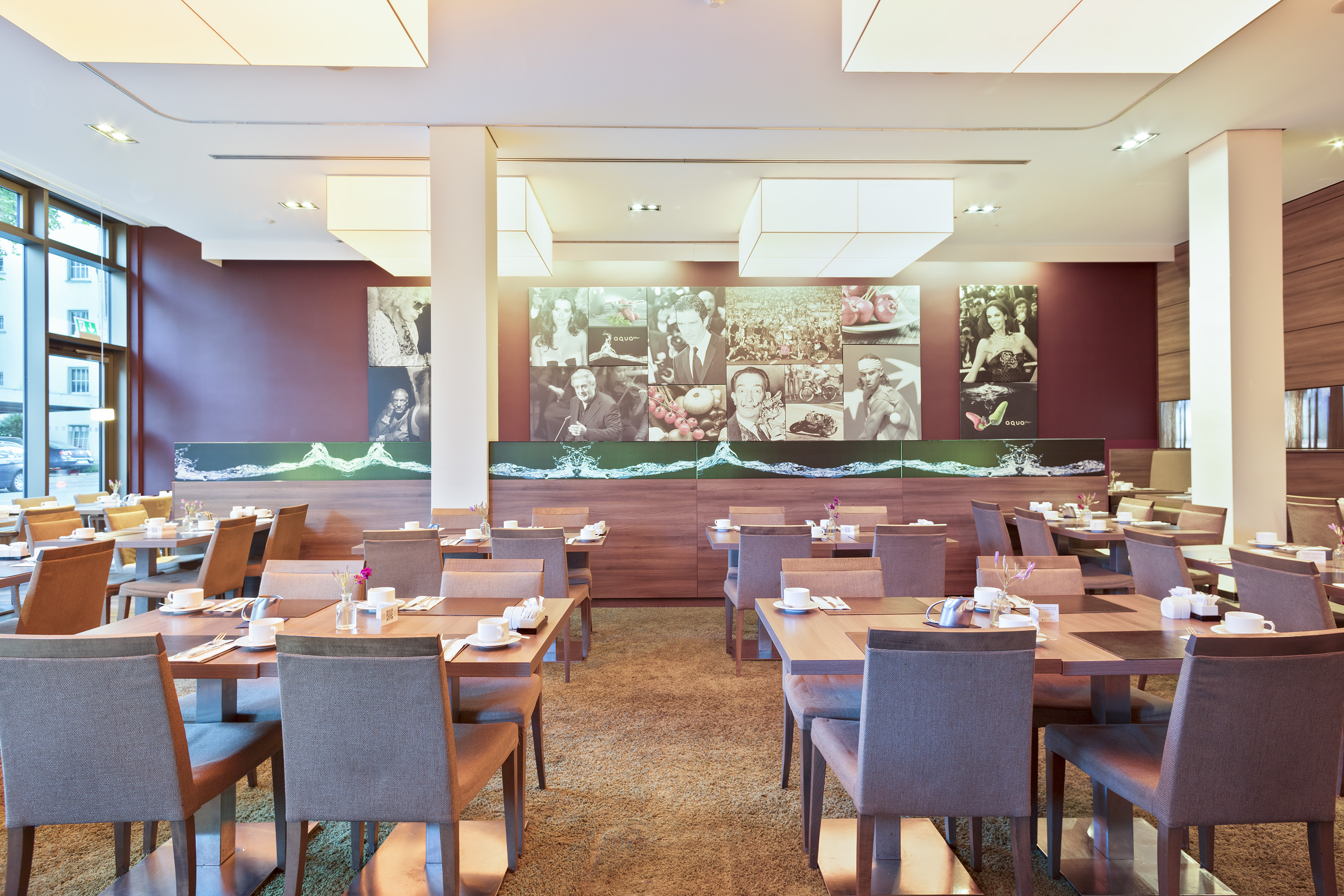 Modern hotel restaurant with set tables, maroon walls, and artistic murals.