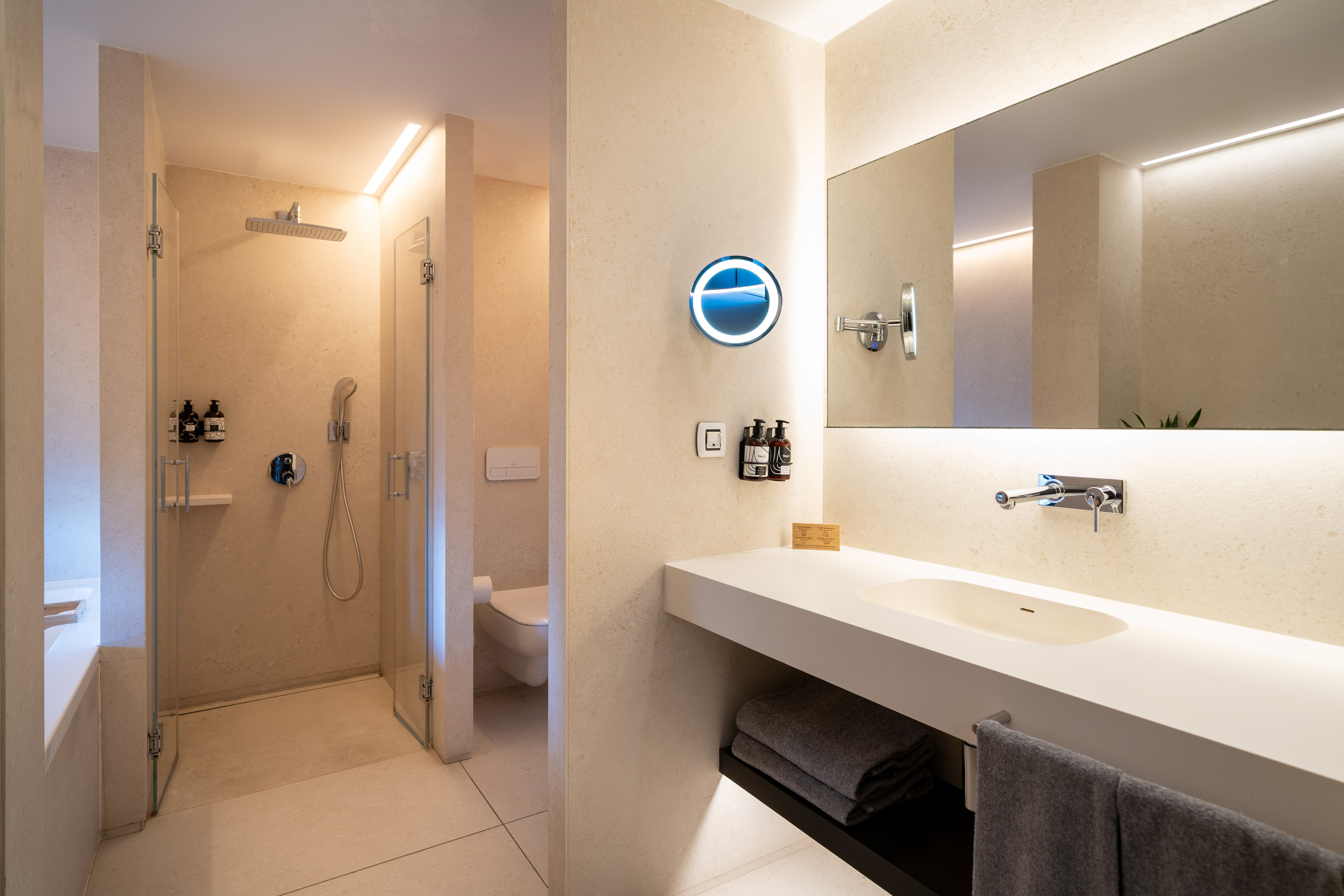 Modern hotel bathroom with walk-in shower, floating vanity, and backlit mirror.
