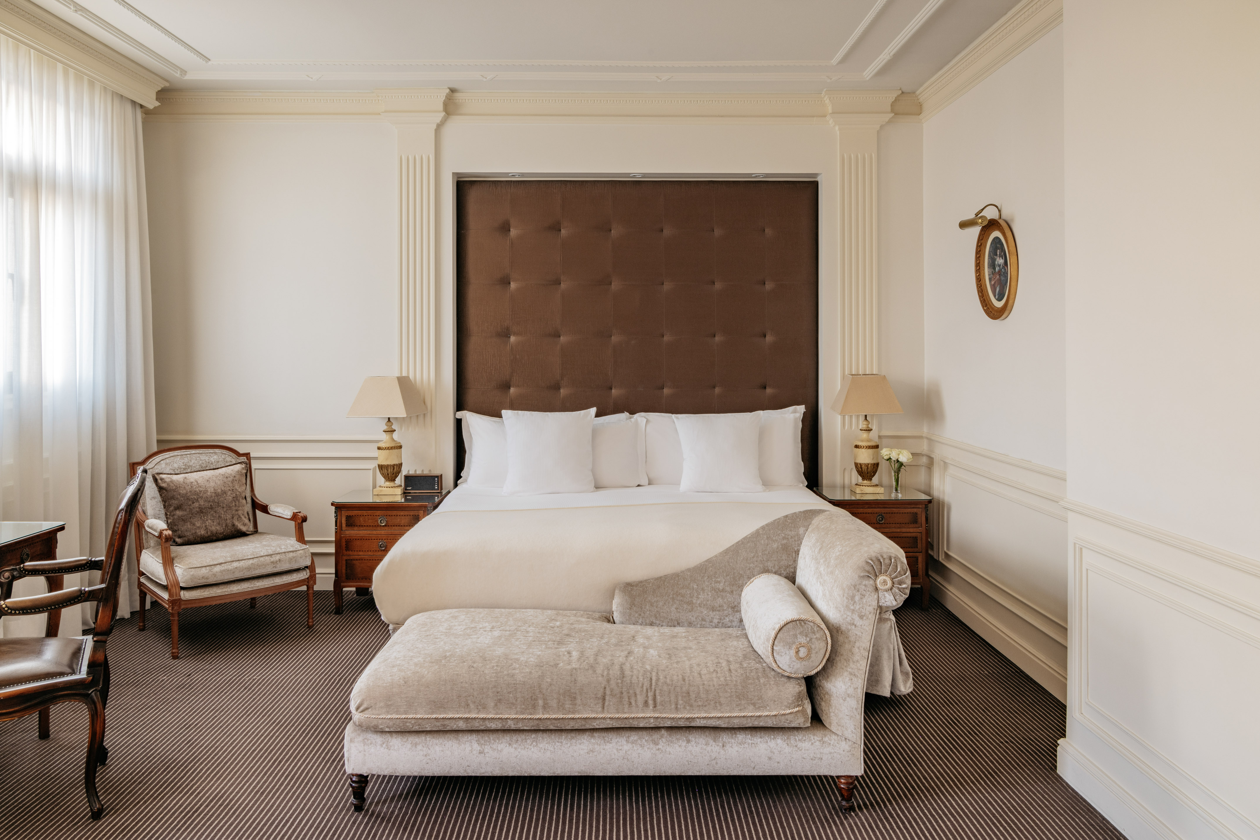 Luxurious hotel bedroom with king bed, chaise lounge, and elegant decor.