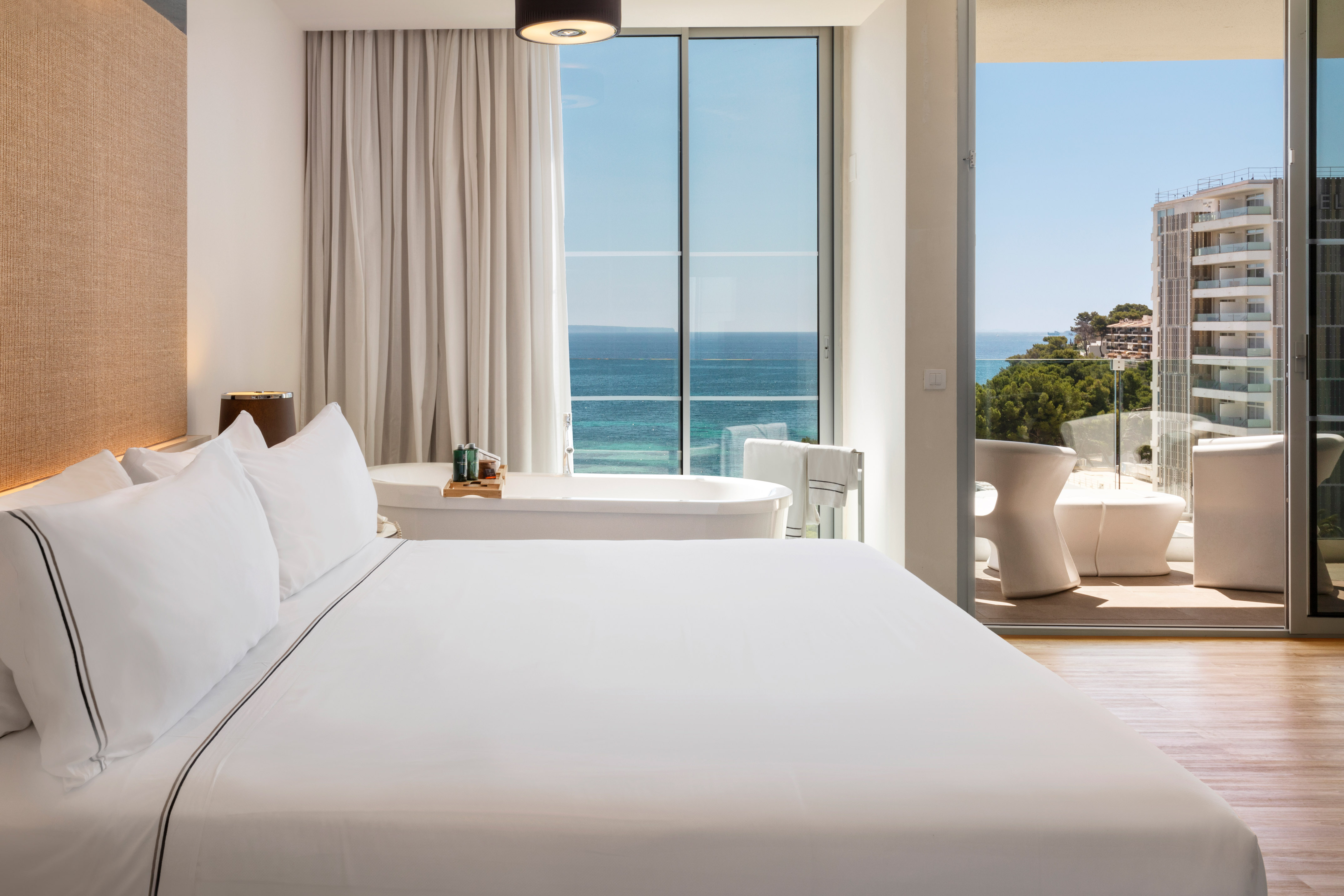 Luxury hotel room with ocean view, freestanding bathtub, and balcony.