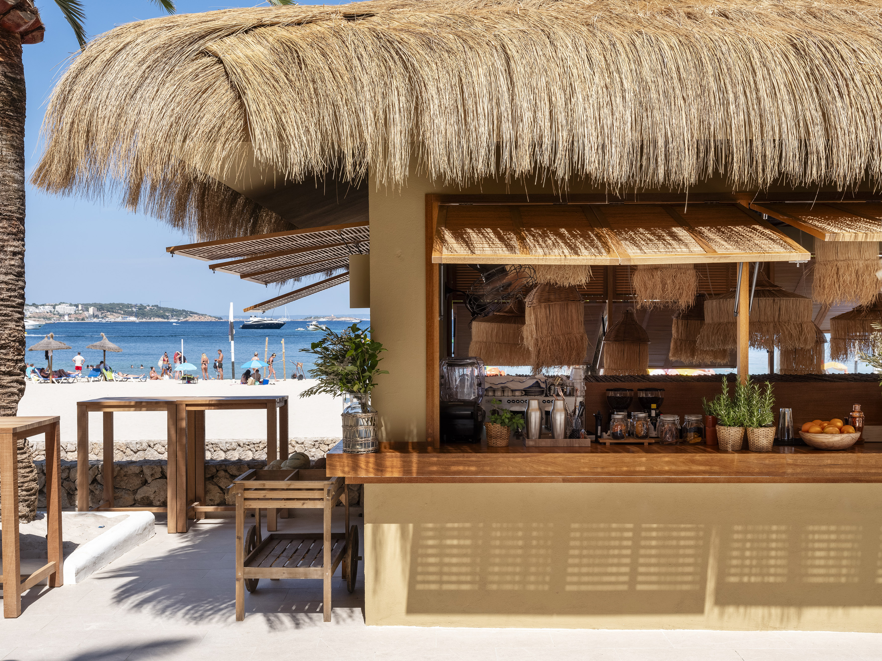 Beachfront tiki bar with thatched roof, wooden counter, ocean view, and people.