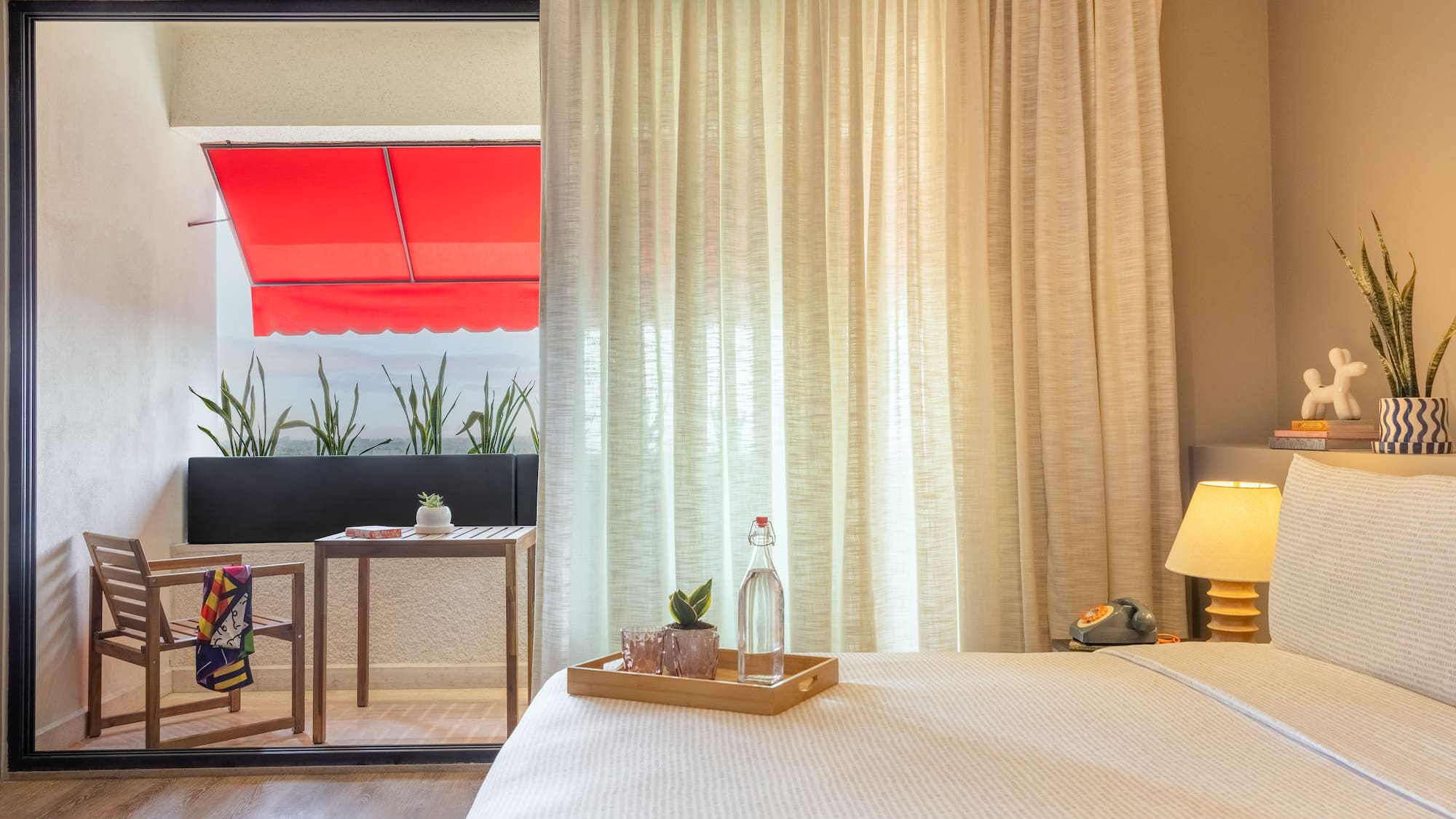 Interior de hotel con cama, balcón con toldo rojo y plantas.