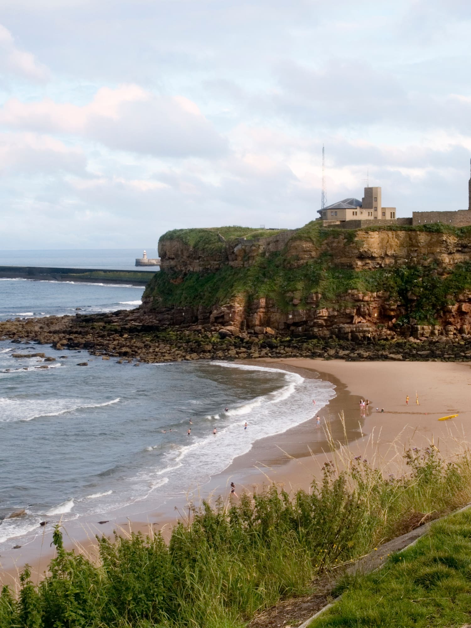 Tynemouth Priory & Castle ruins on cliff, sandy beach below, lighthouse.