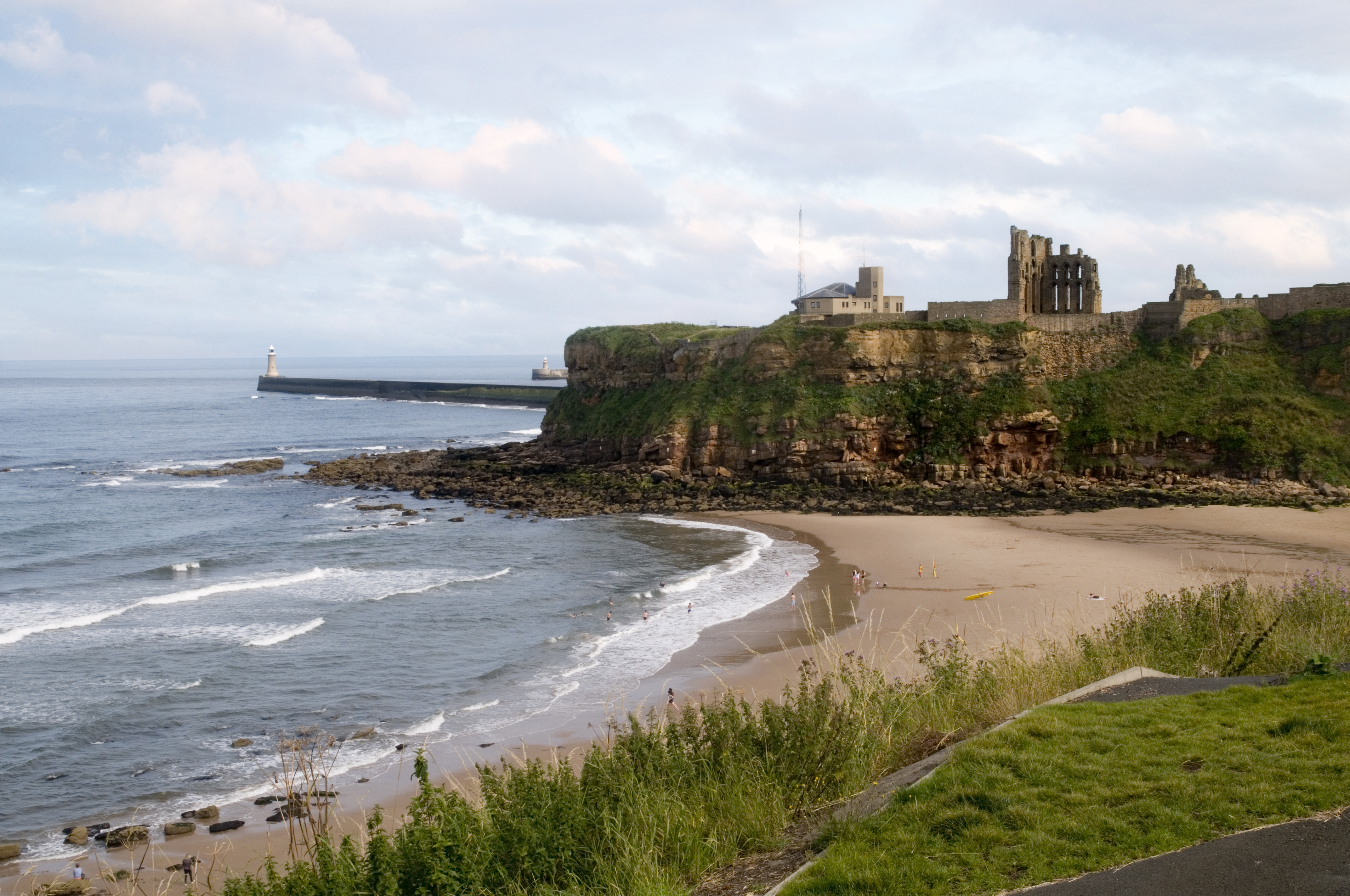 Tynemouth Priory & Castle ruins on cliff, sandy beach below, lighthouse.