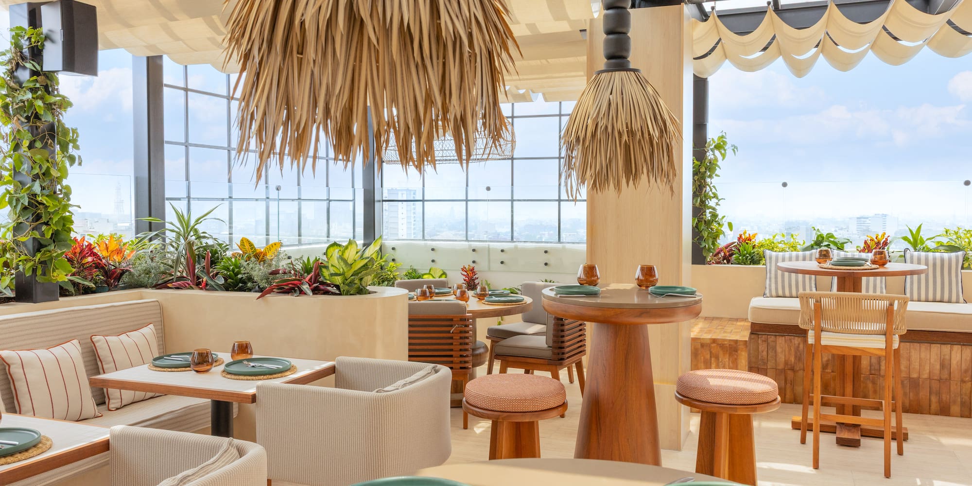 Rooftop restaurant with city view, lush plants, modern seating, and straw light fixtures.