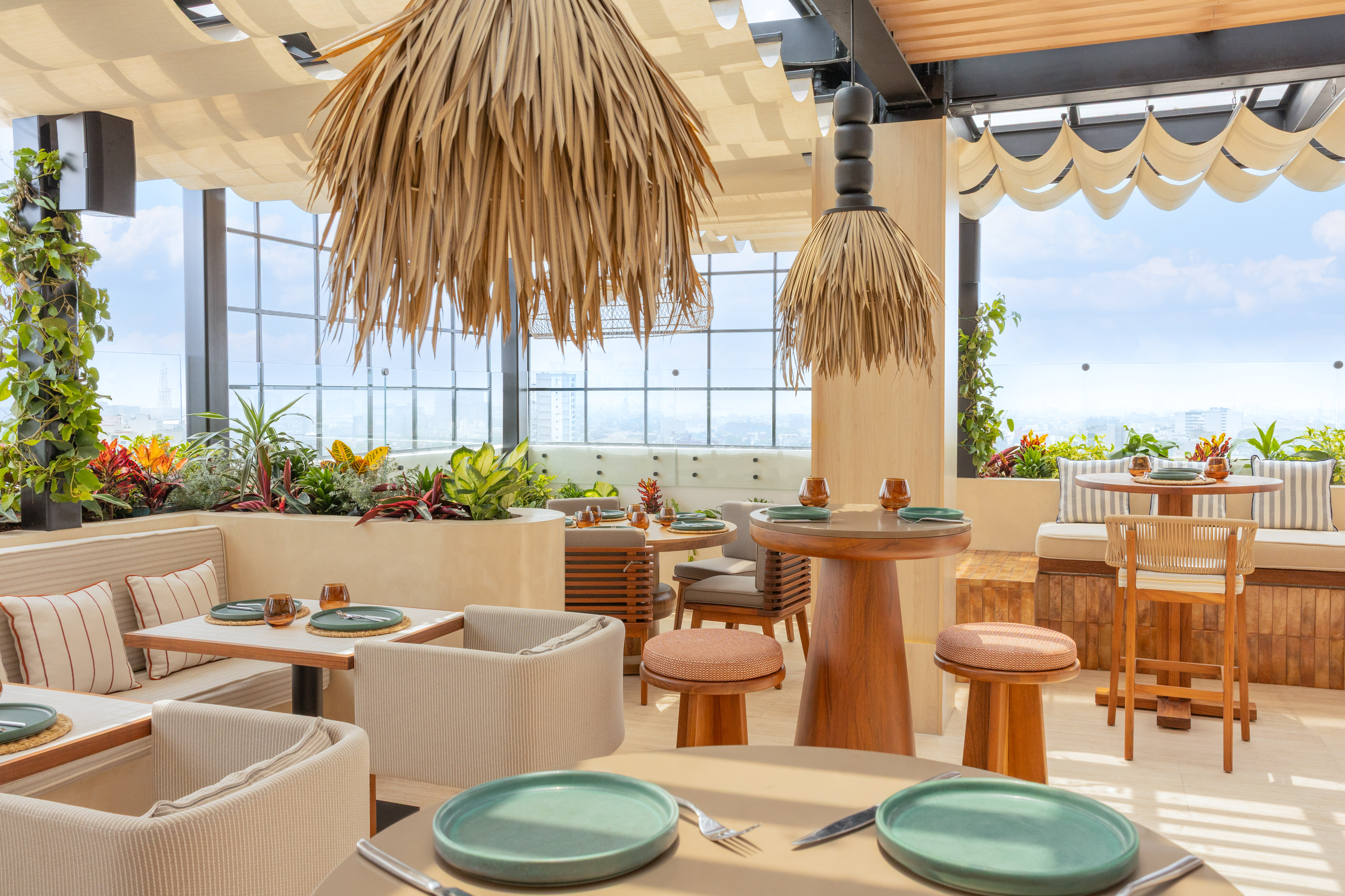Rooftop restaurant with city view, lush plants, modern seating, and straw light fixtures.