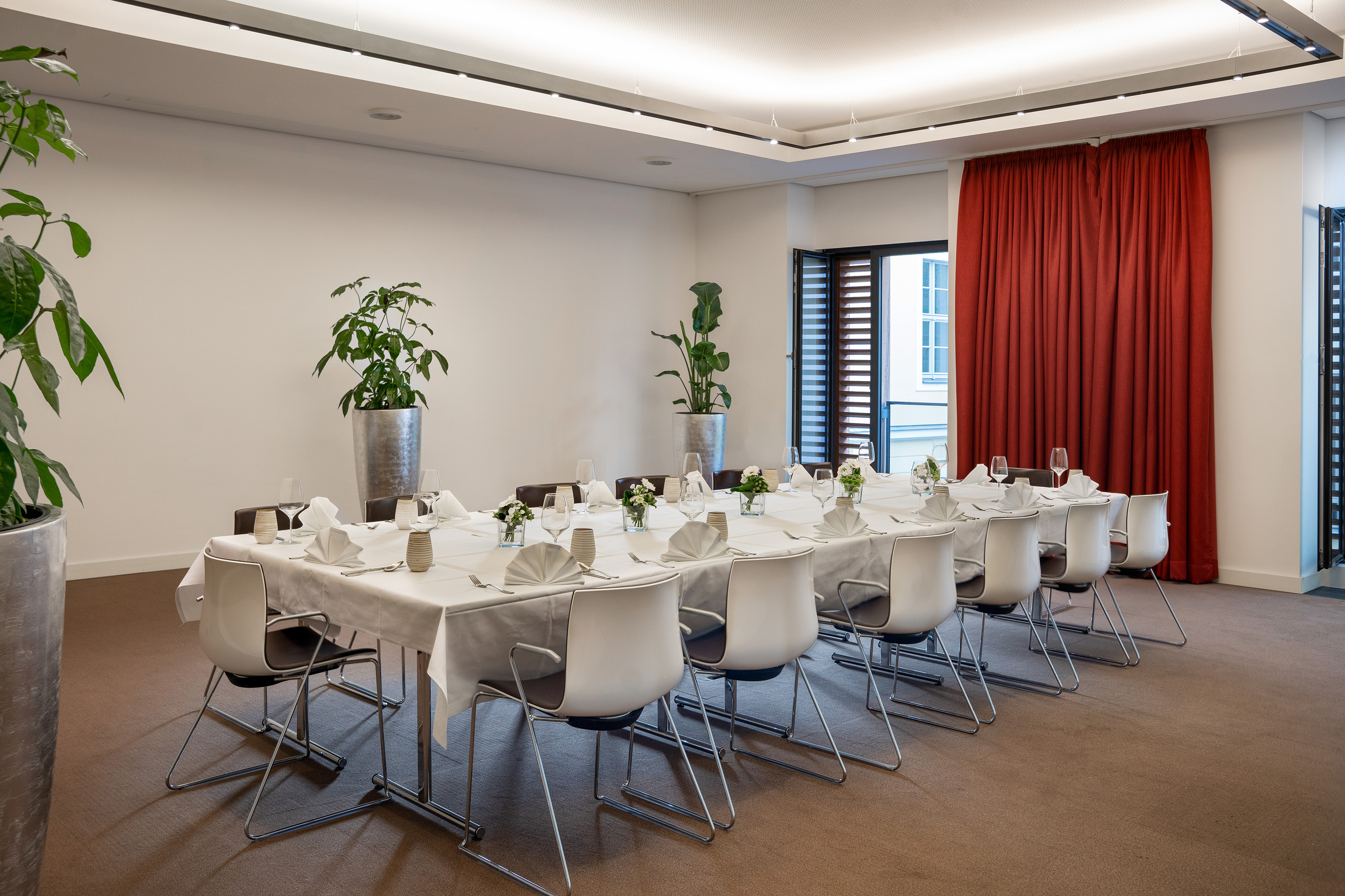 Modern meeting room with long dining table, white settings, and red curtains. - CONEins - Innside Dresda, Dresda