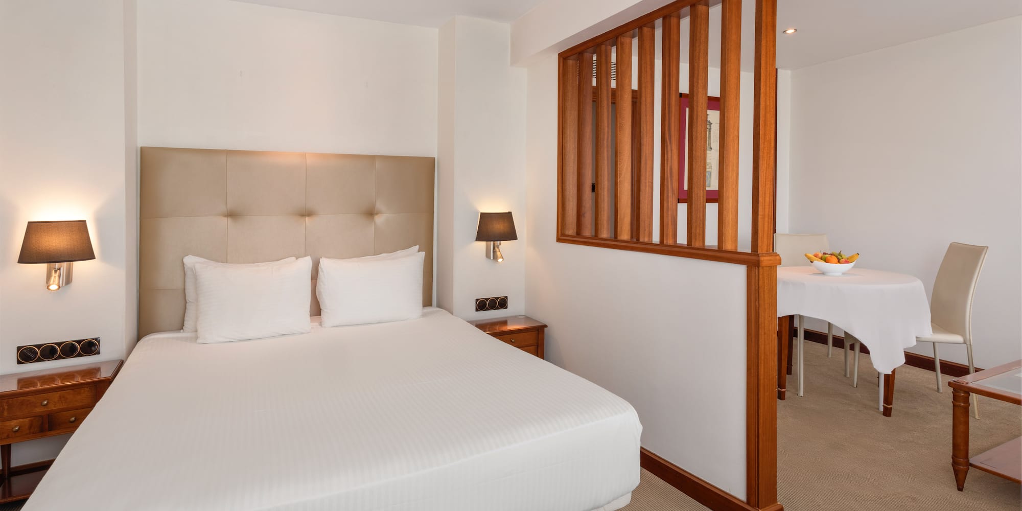 Comfortable hotel suite with queen bed and adjacent dining area.