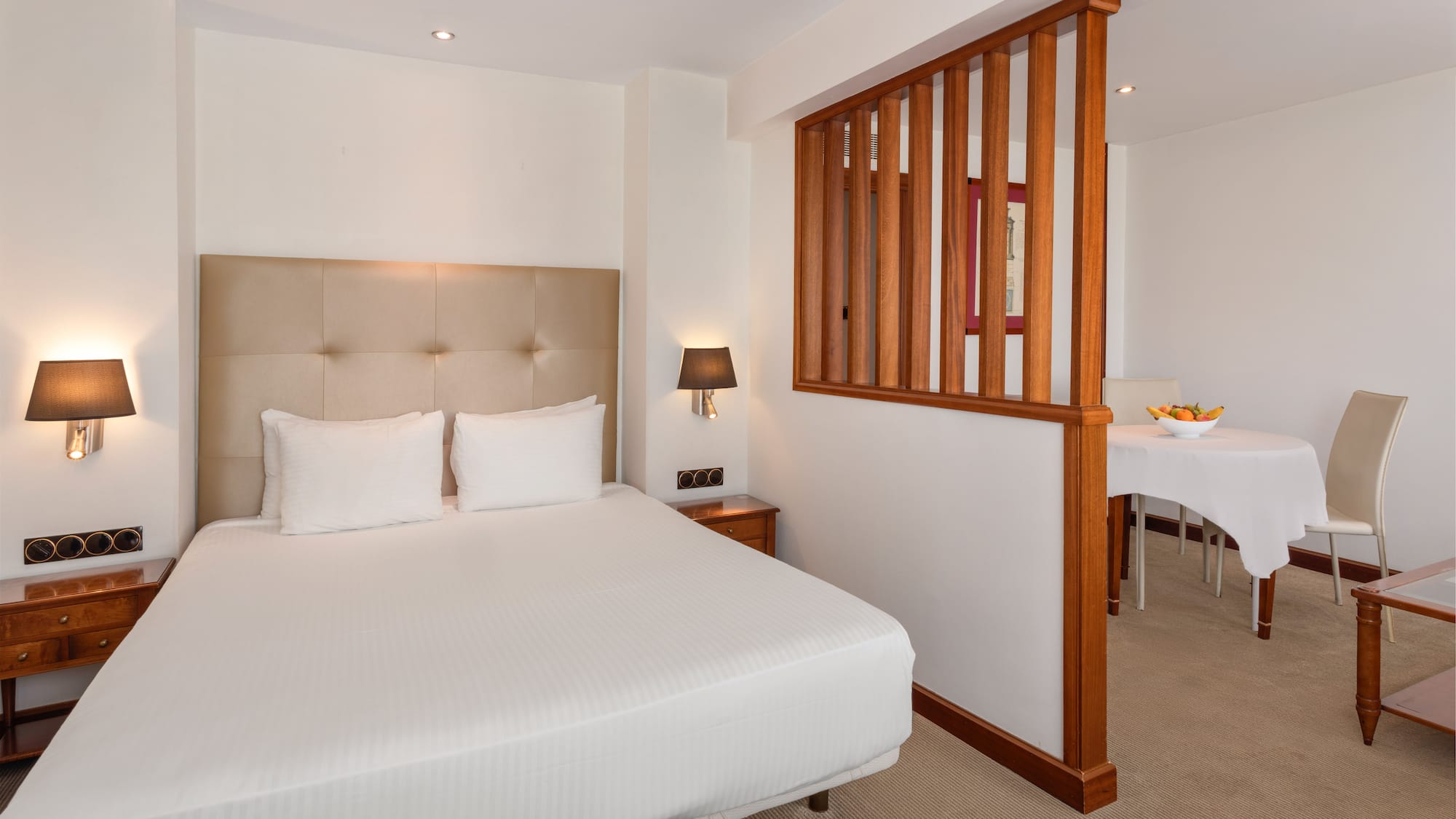 Comfortable hotel suite with queen bed and adjacent dining area.