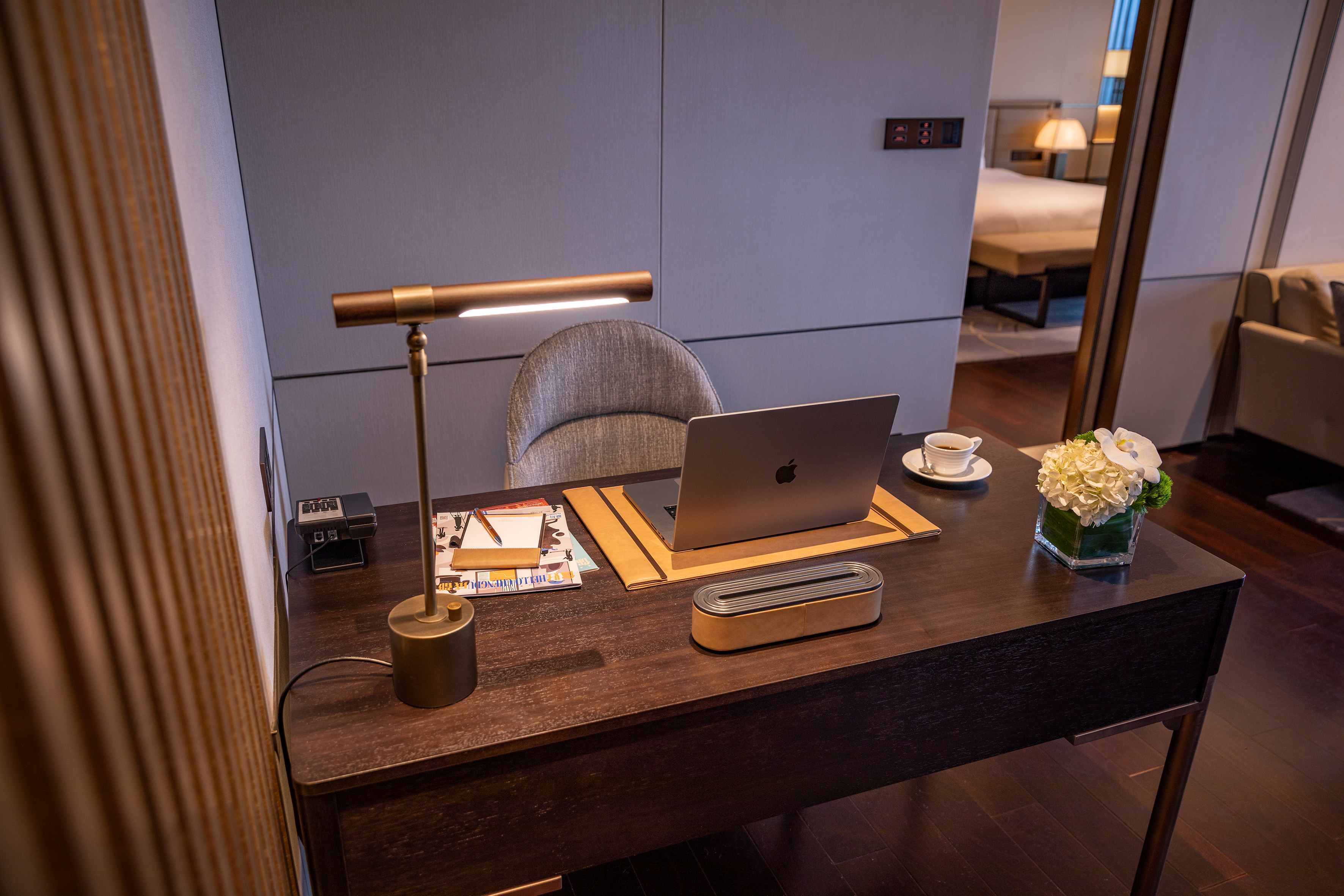 Modern hotel workspace: laptop, bronze lamp, coffee on dark wood desk.