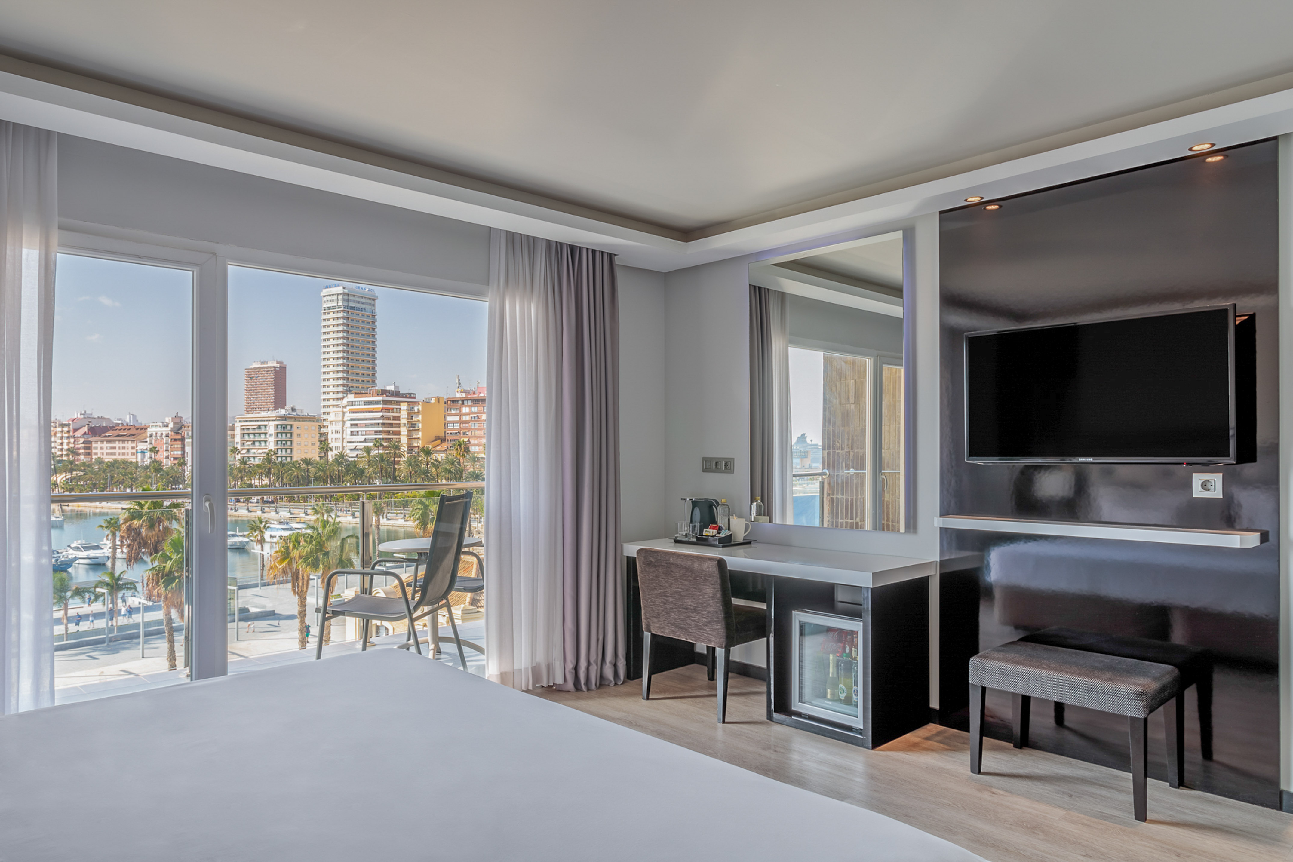 Modern hotel room with balcony overlooking marina and city skyline.