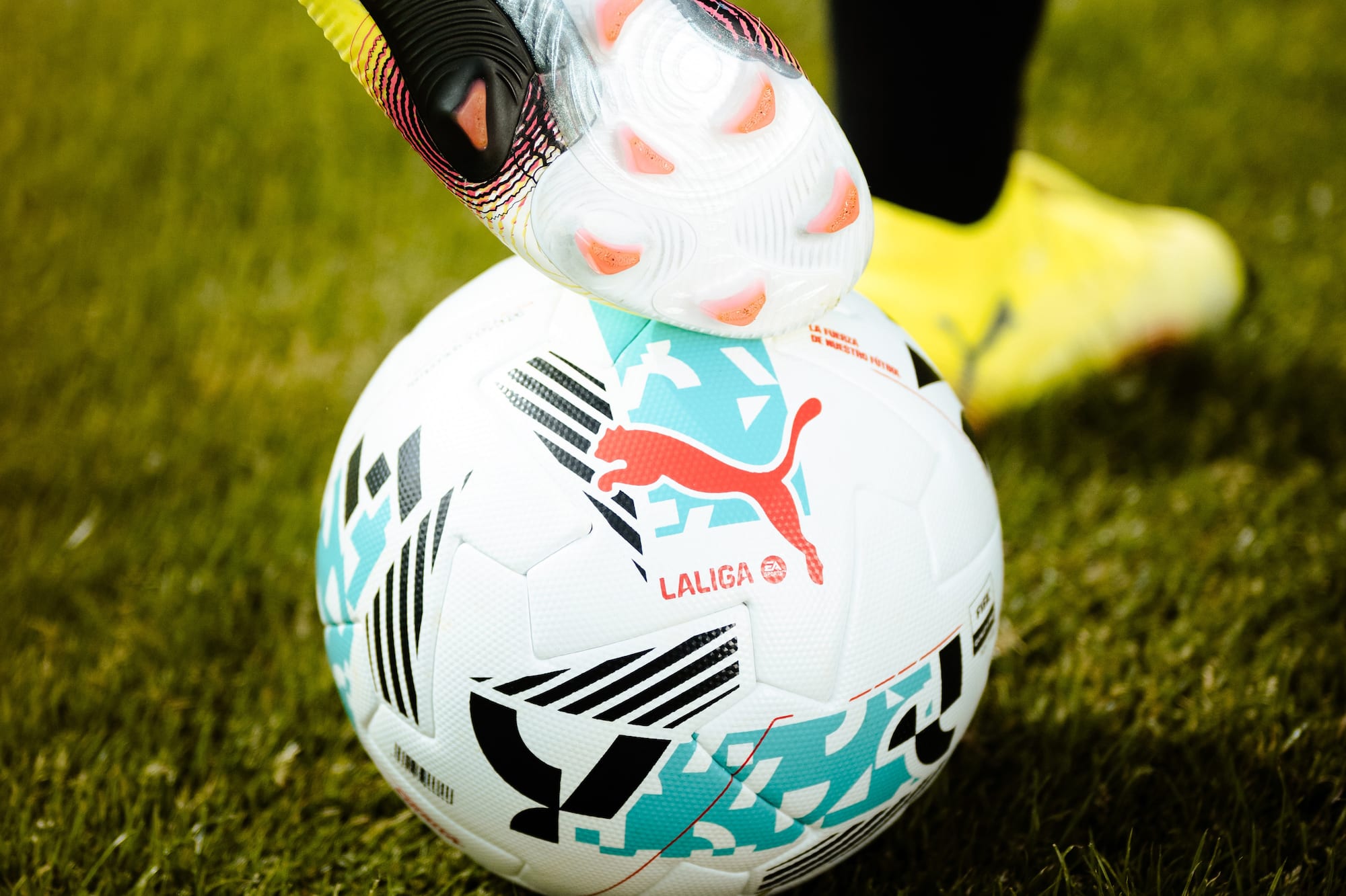 Soccer cleat on Puma LaLiga football on green grass.
