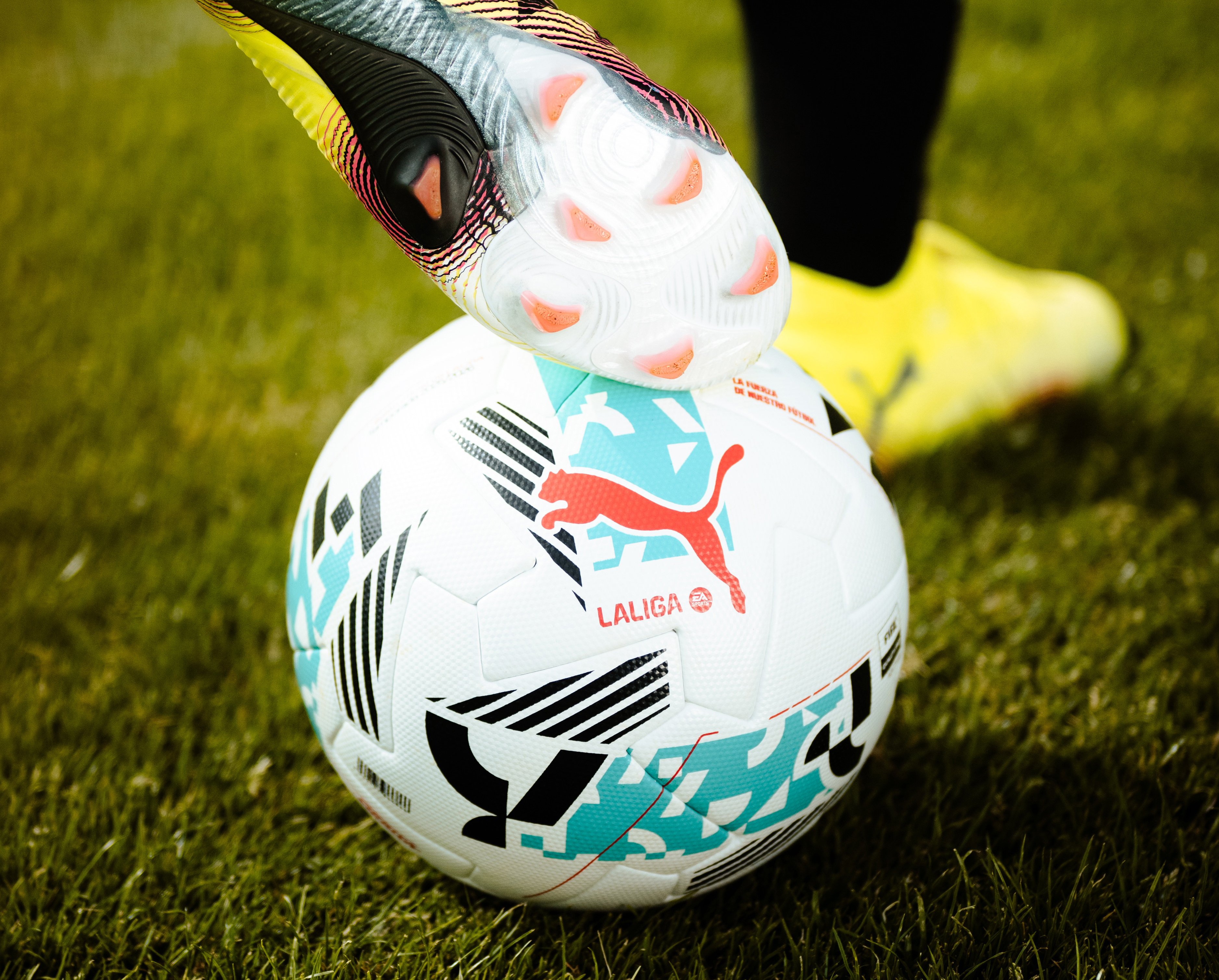 Soccer cleat on Puma LaLiga football on green grass.