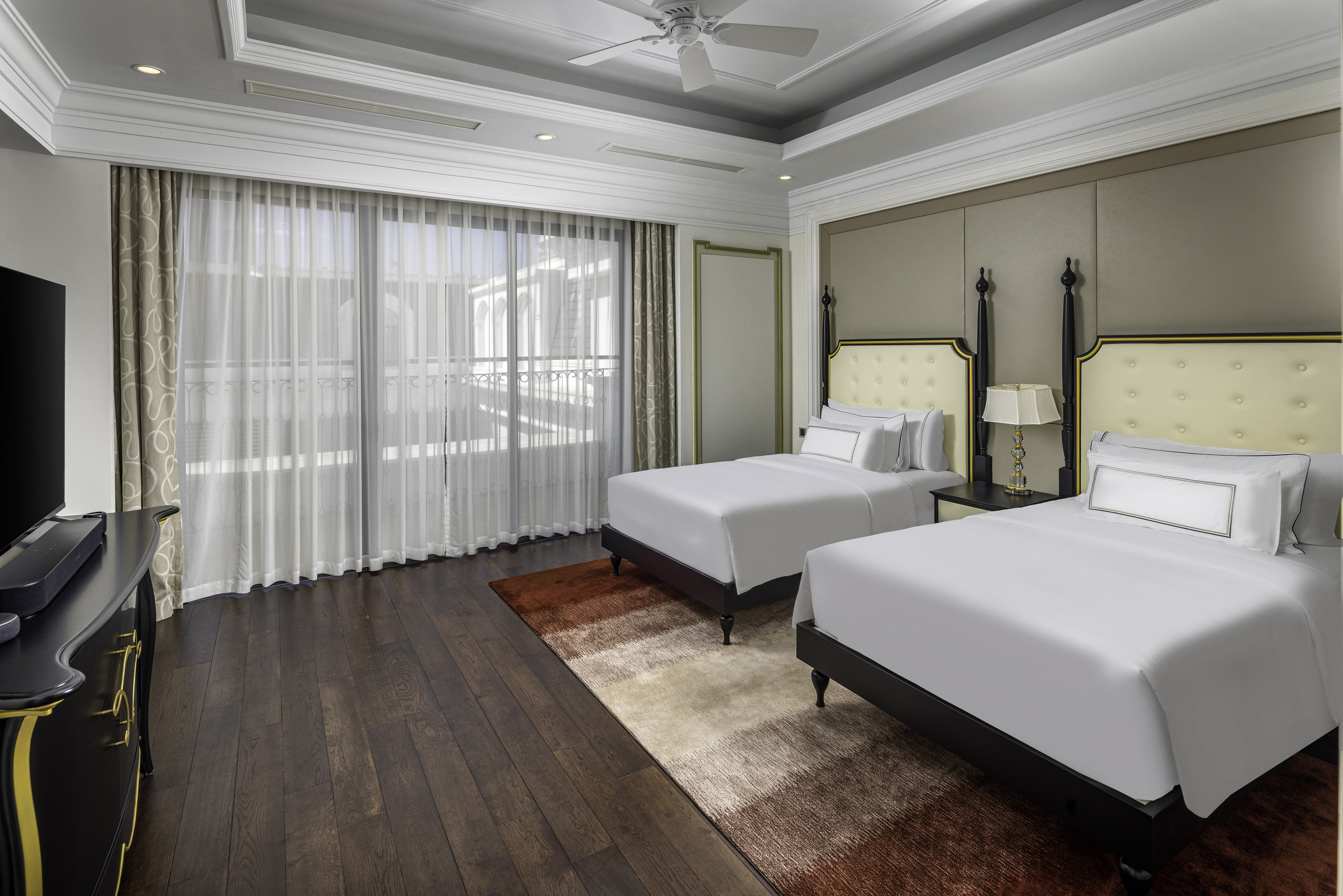 Luxury hotel room with two twin beds, dark wood floor, window, and gradient rug.